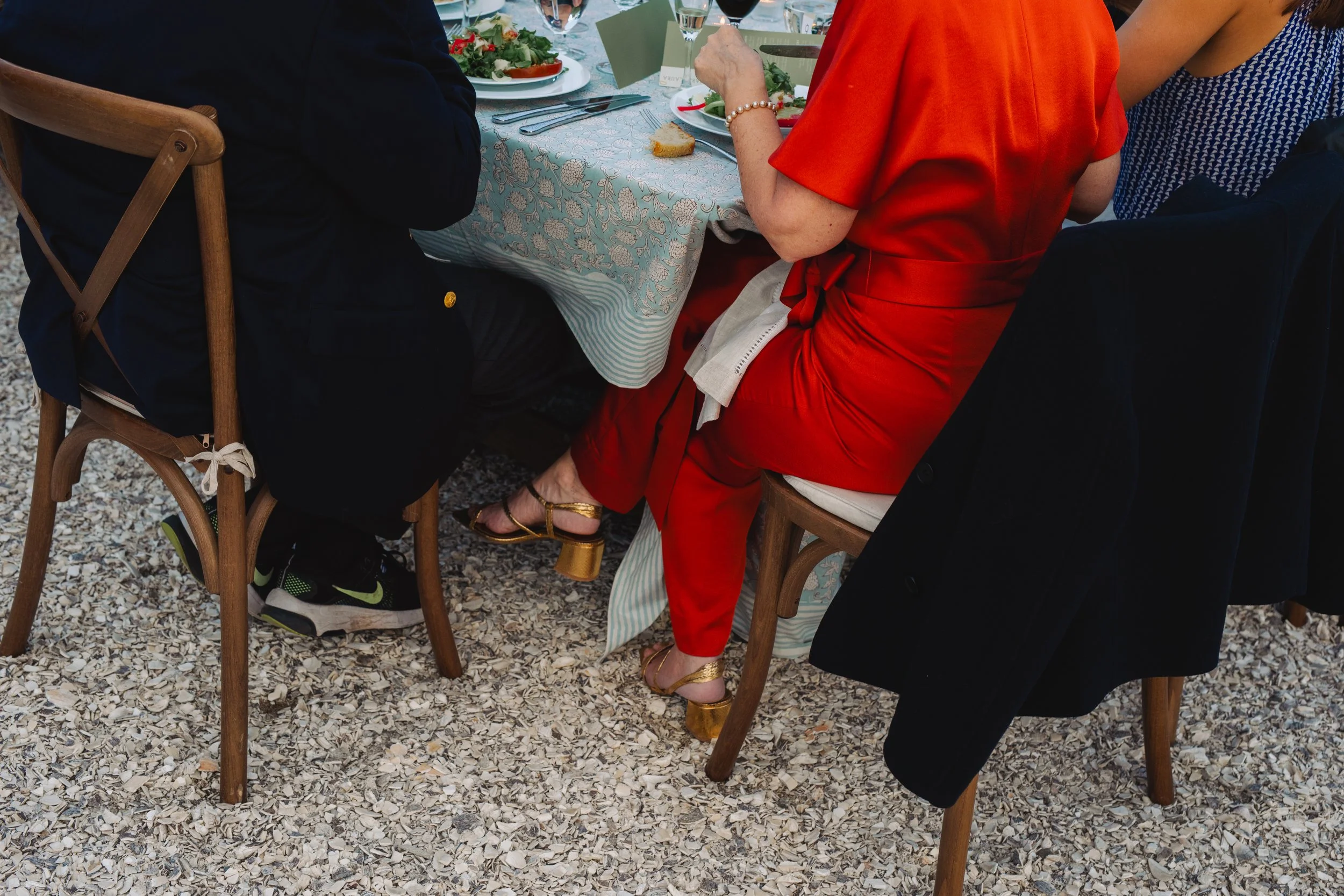 The wedding dinner is in full swing and 2 quests are siting on wood chairs as food is served.