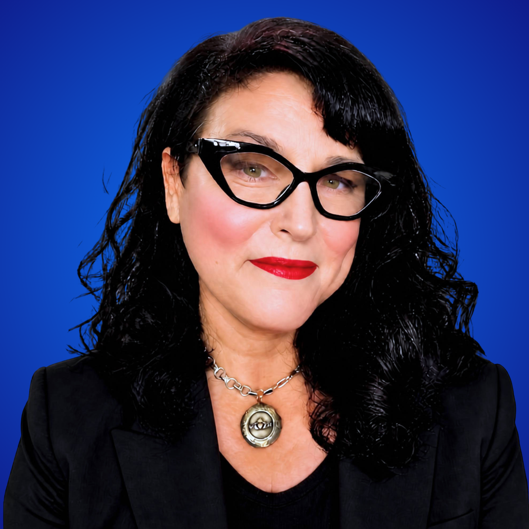 A woman with black hair and glasses, wearing dark lipstick and a necklace, against a blue background.