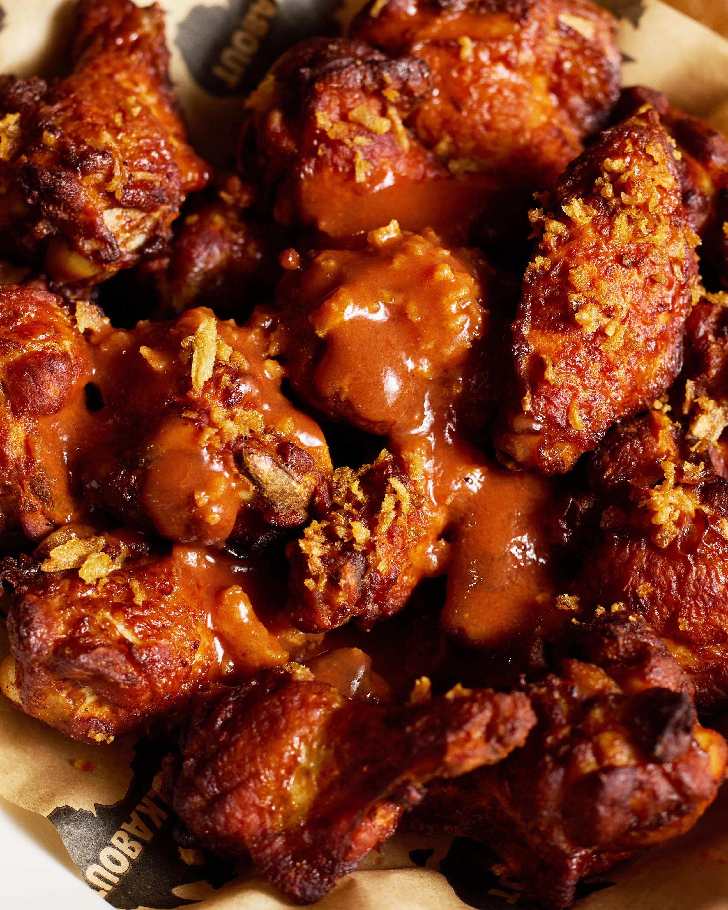 Close-up of spicy buffalo chicken wings coated with barbecue sauce and sprinkled with crushed crispy toppings.
