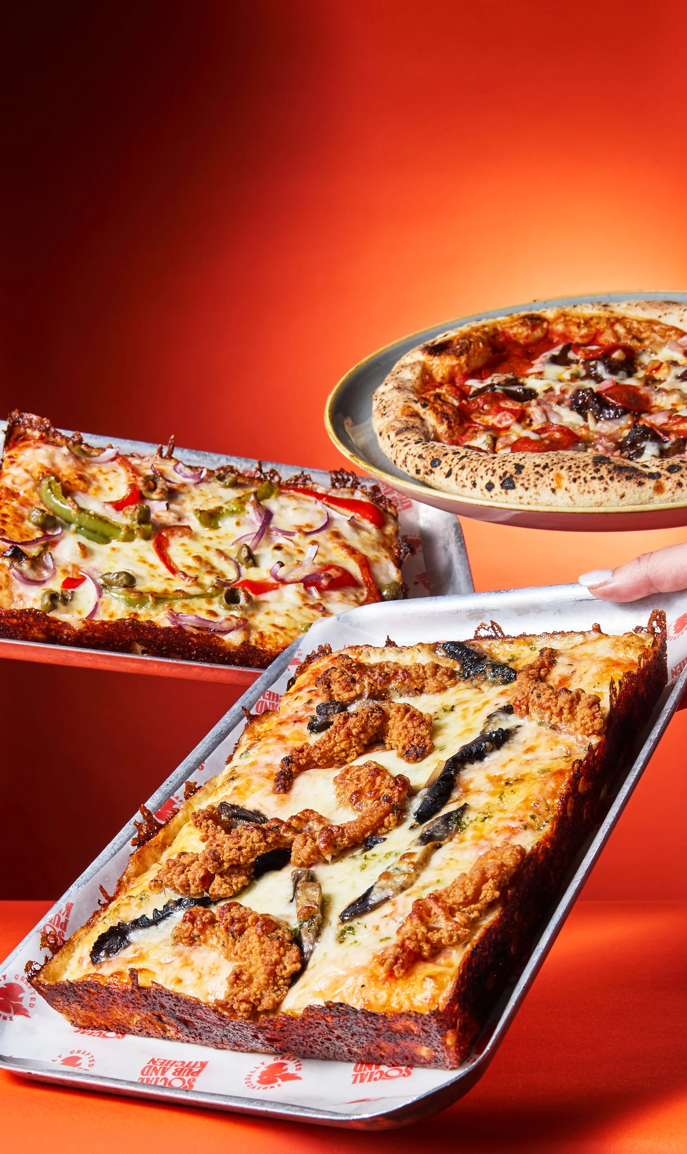 Three different pizzas and a cheesy breadstick on a red background.