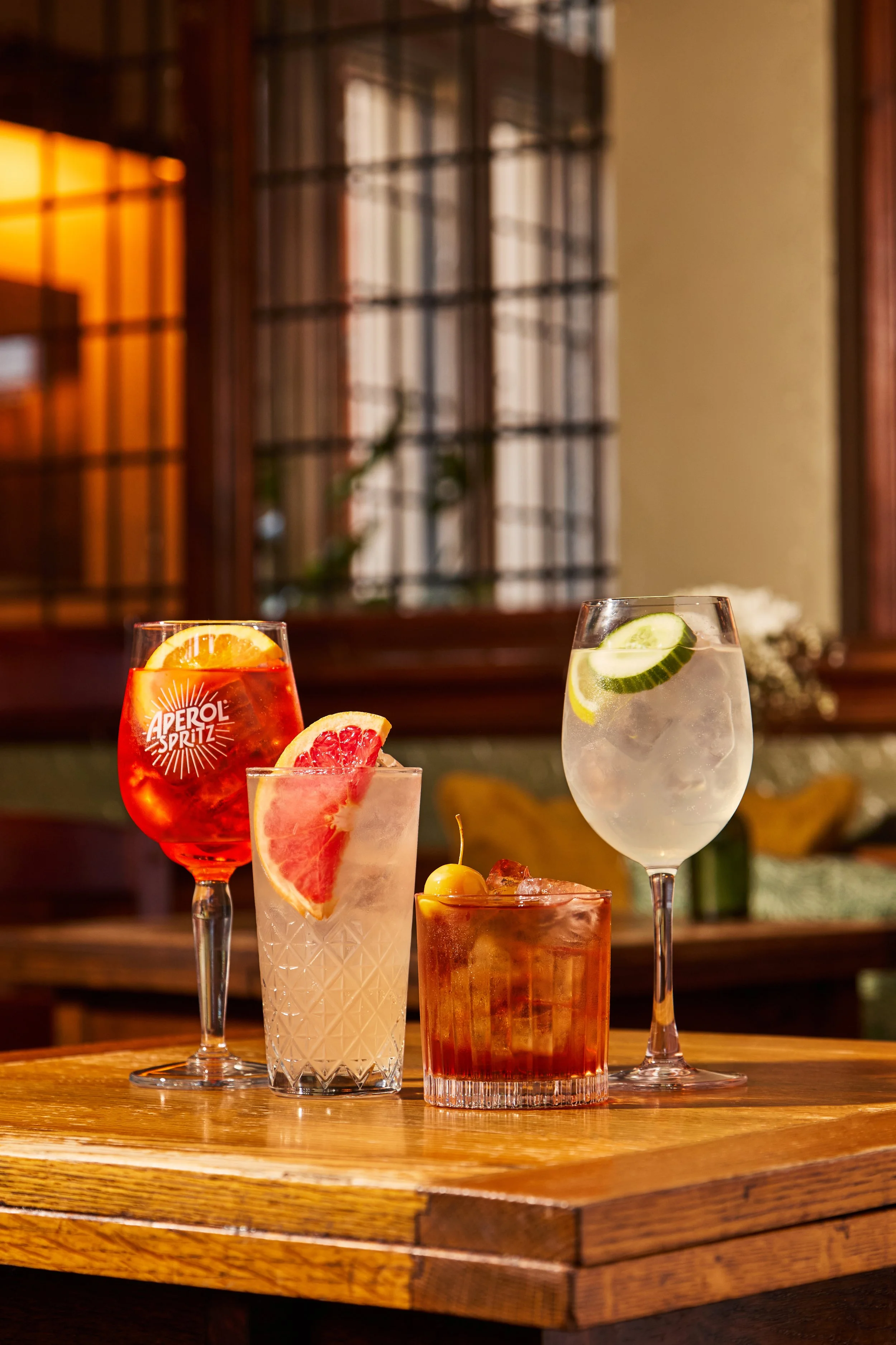 Four colorful cocktails with garnishes on a wooden table in a cozy indoor setting.