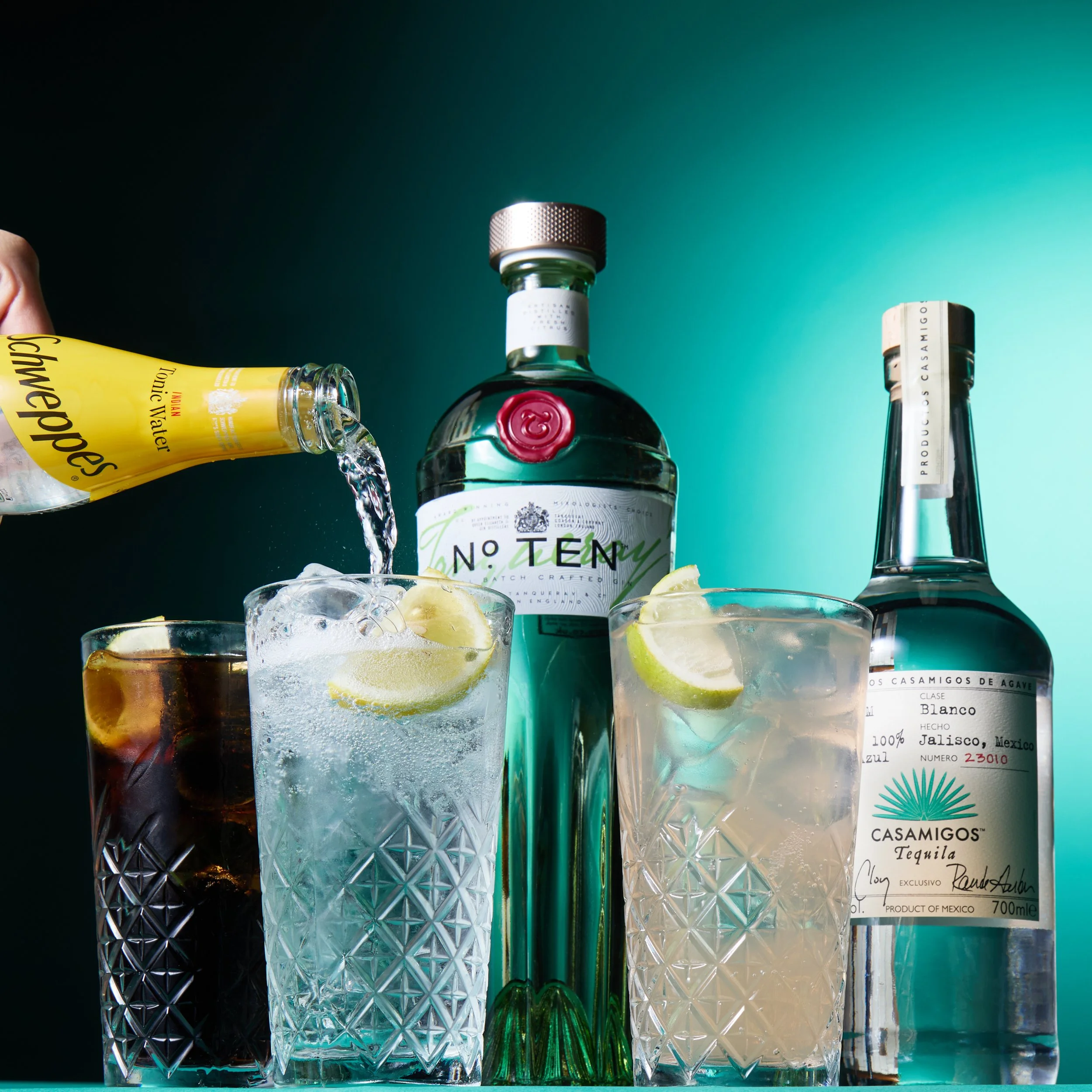  assortment of tequila bottles and three glasses with ice and lime wedges, one being poured with tonic water