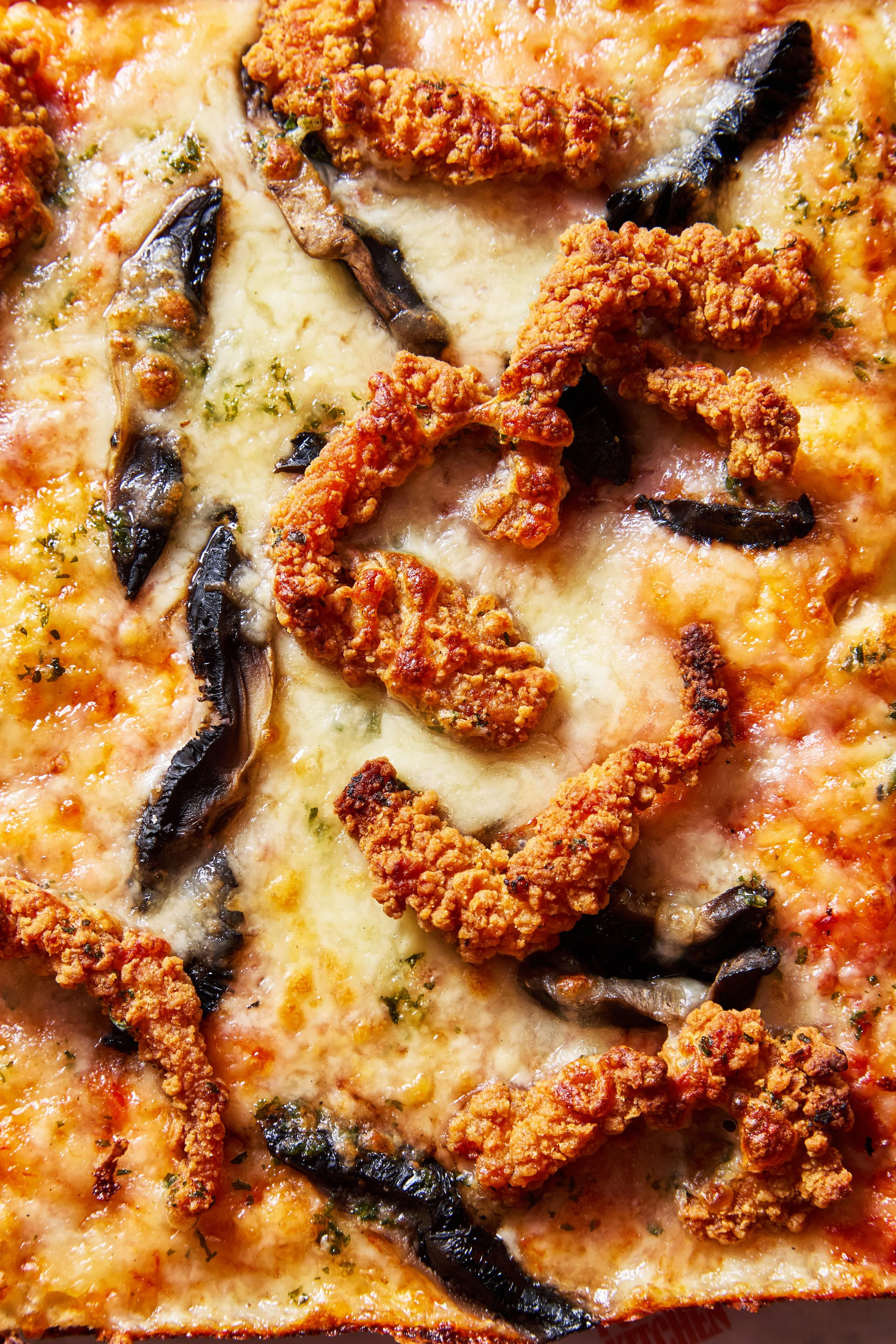 Close-up of a pizza with cheese, fried chicken pieces, black olives, and herbs.