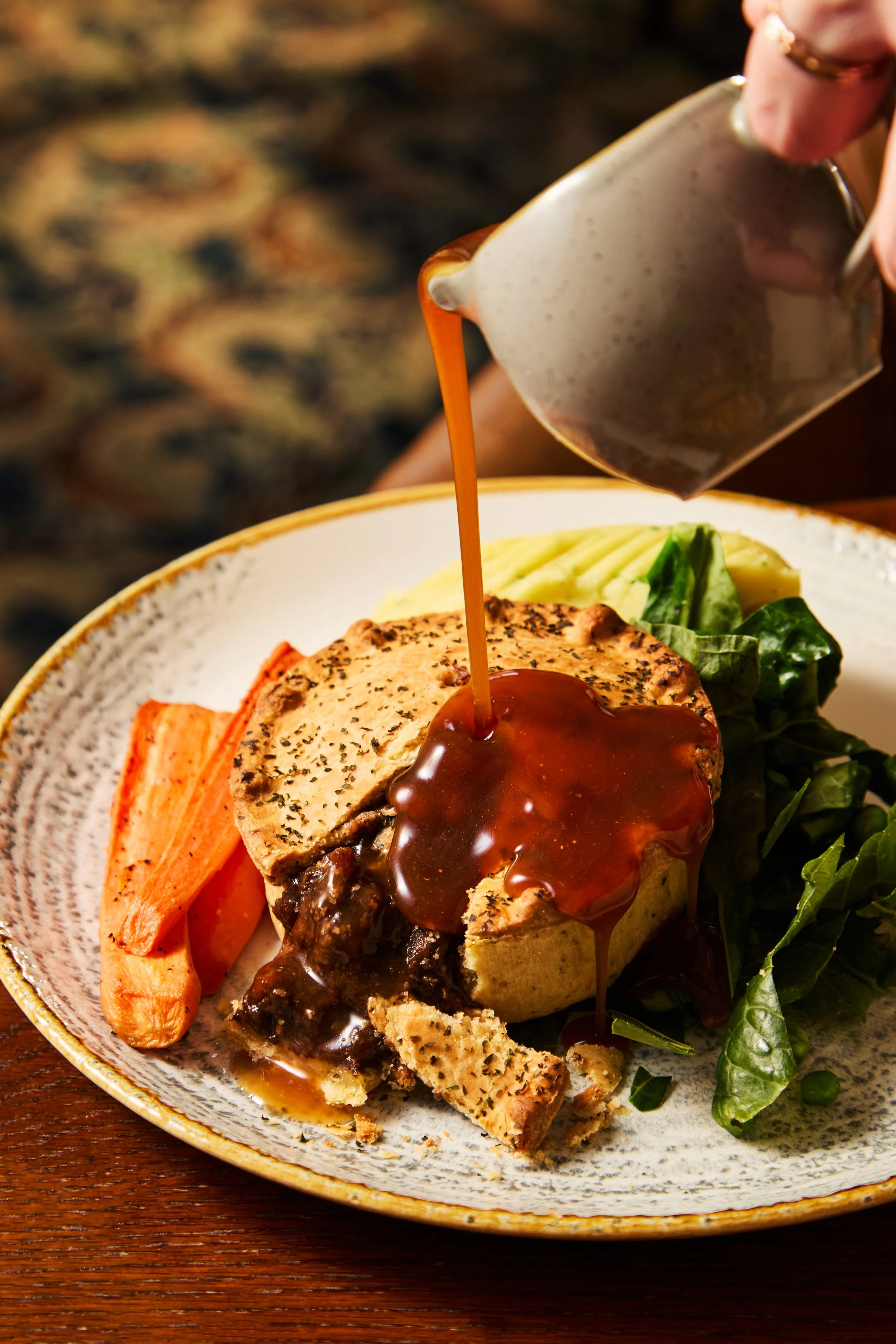 A plate with a cooked meat dish topped with gravy, roasted carrots, and served with fresh green salad, on a wooden table.