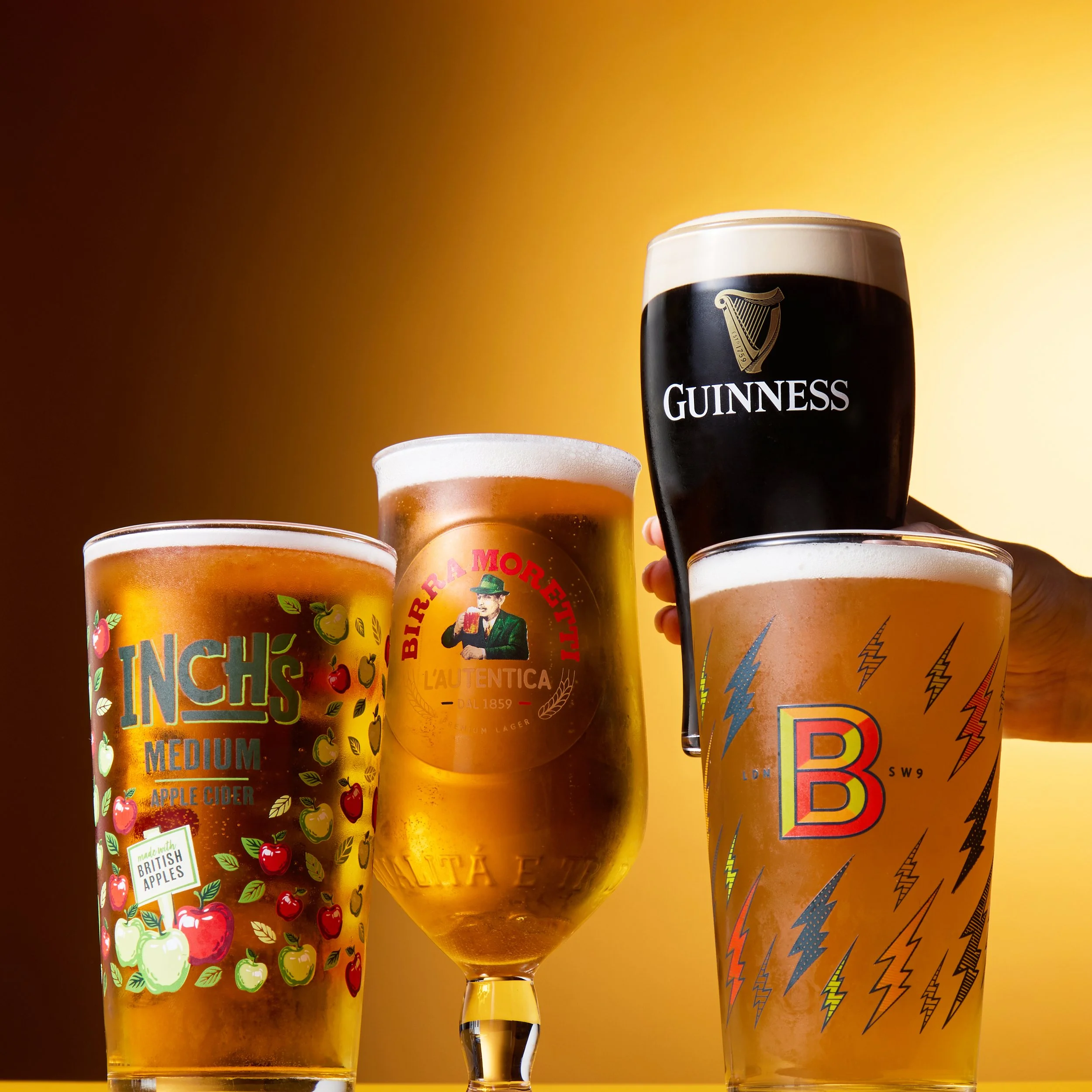 Four glasses of beer, including Guinness, arranged against a gradient background with shades of brown and gold.