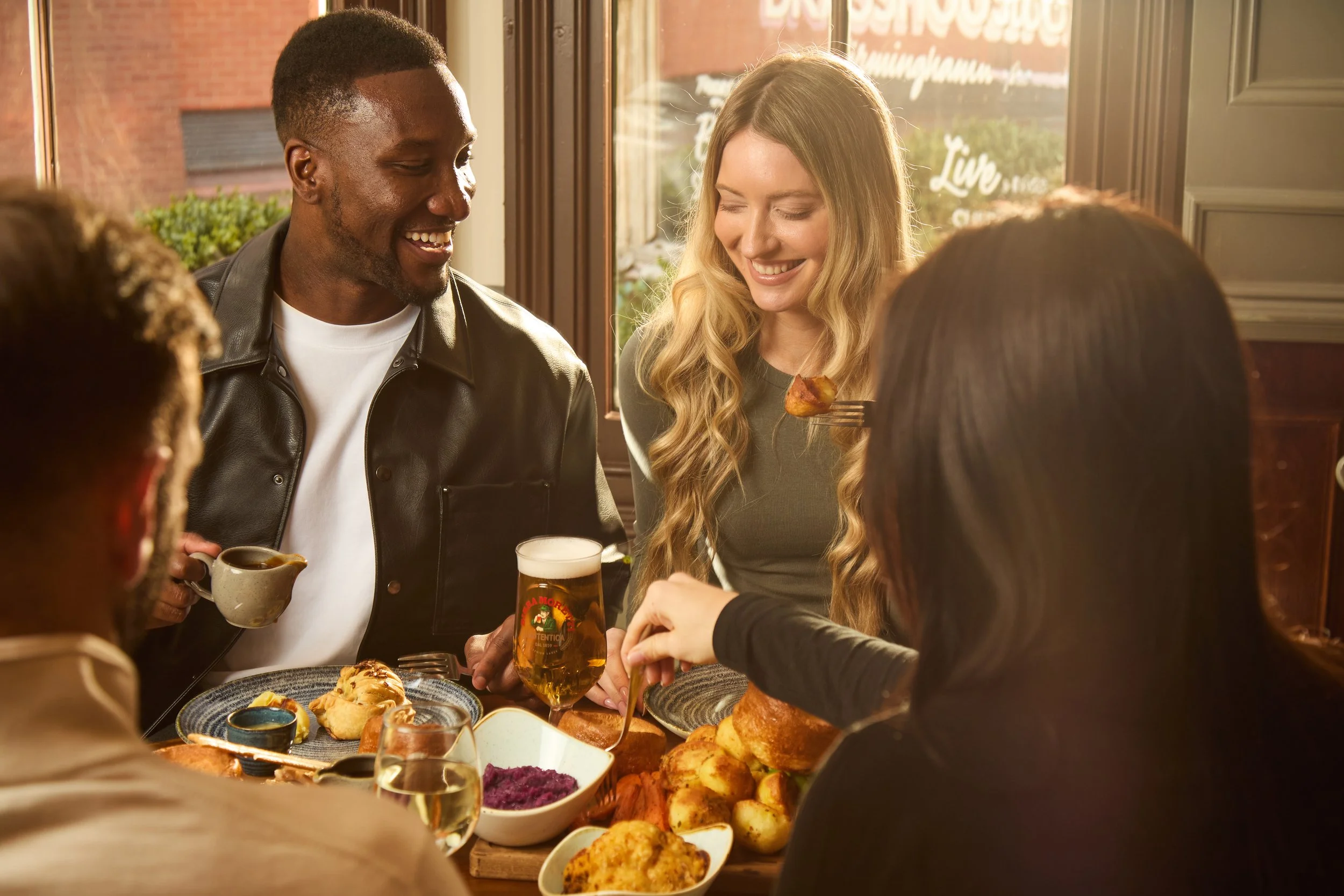 People gathering around a table with food and drinks inside a restaurant, smiling and enjoying themselves.