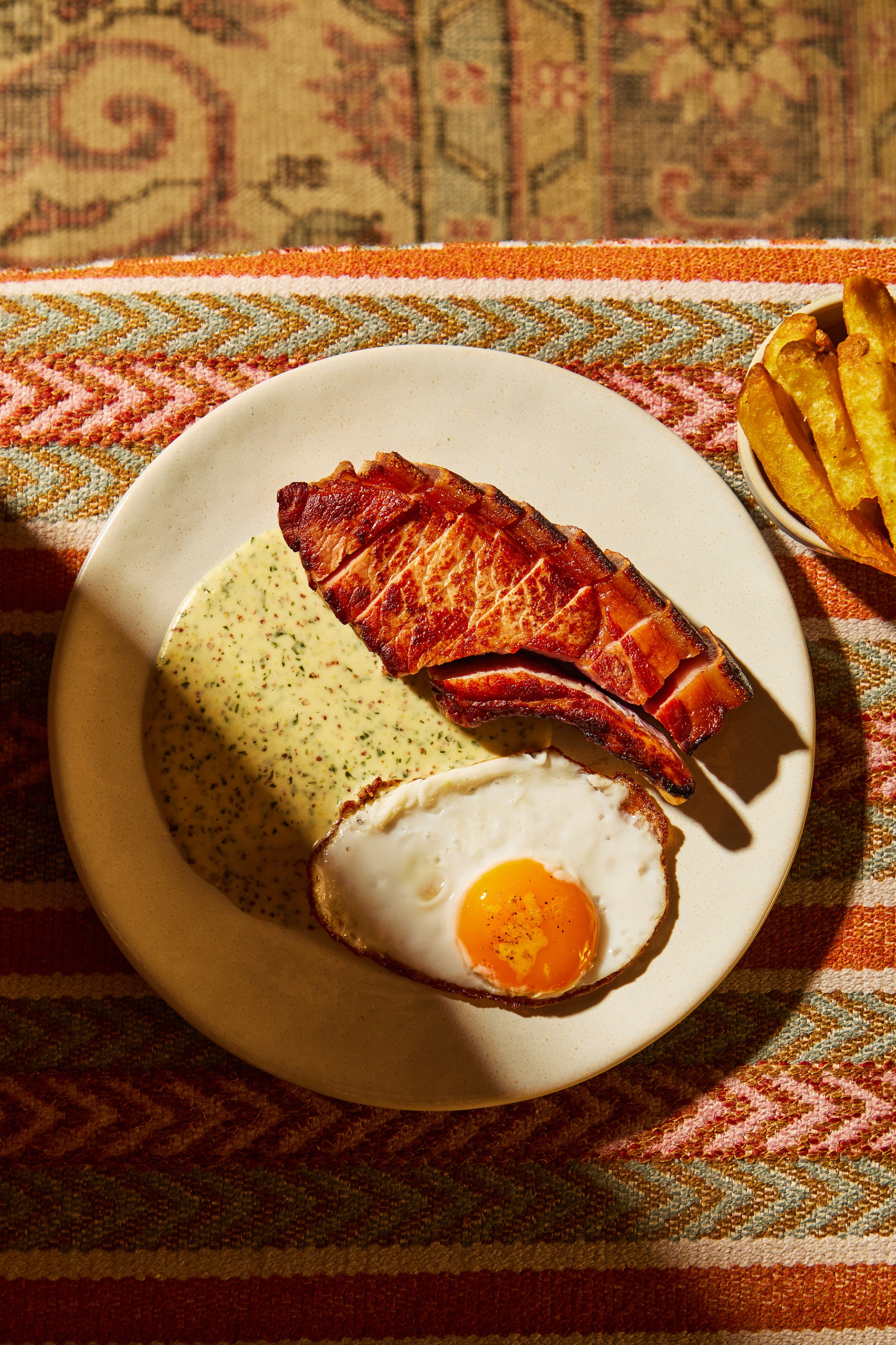 A breakfast plate with bacon, a fried egg, and herb-seasoned sauce, with a side of French fries.