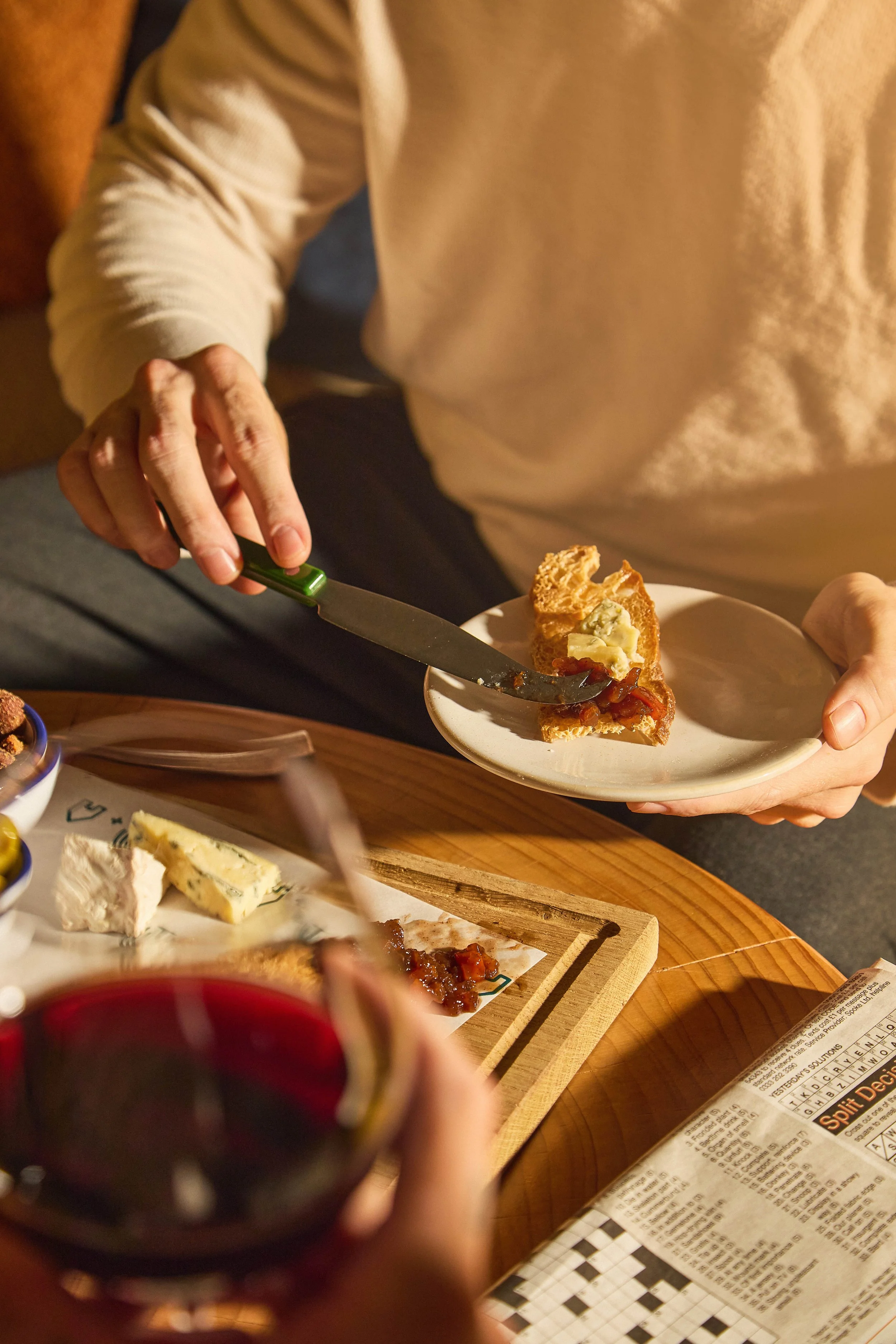Person holding a glass of red wine with a meal and cheese on the table.