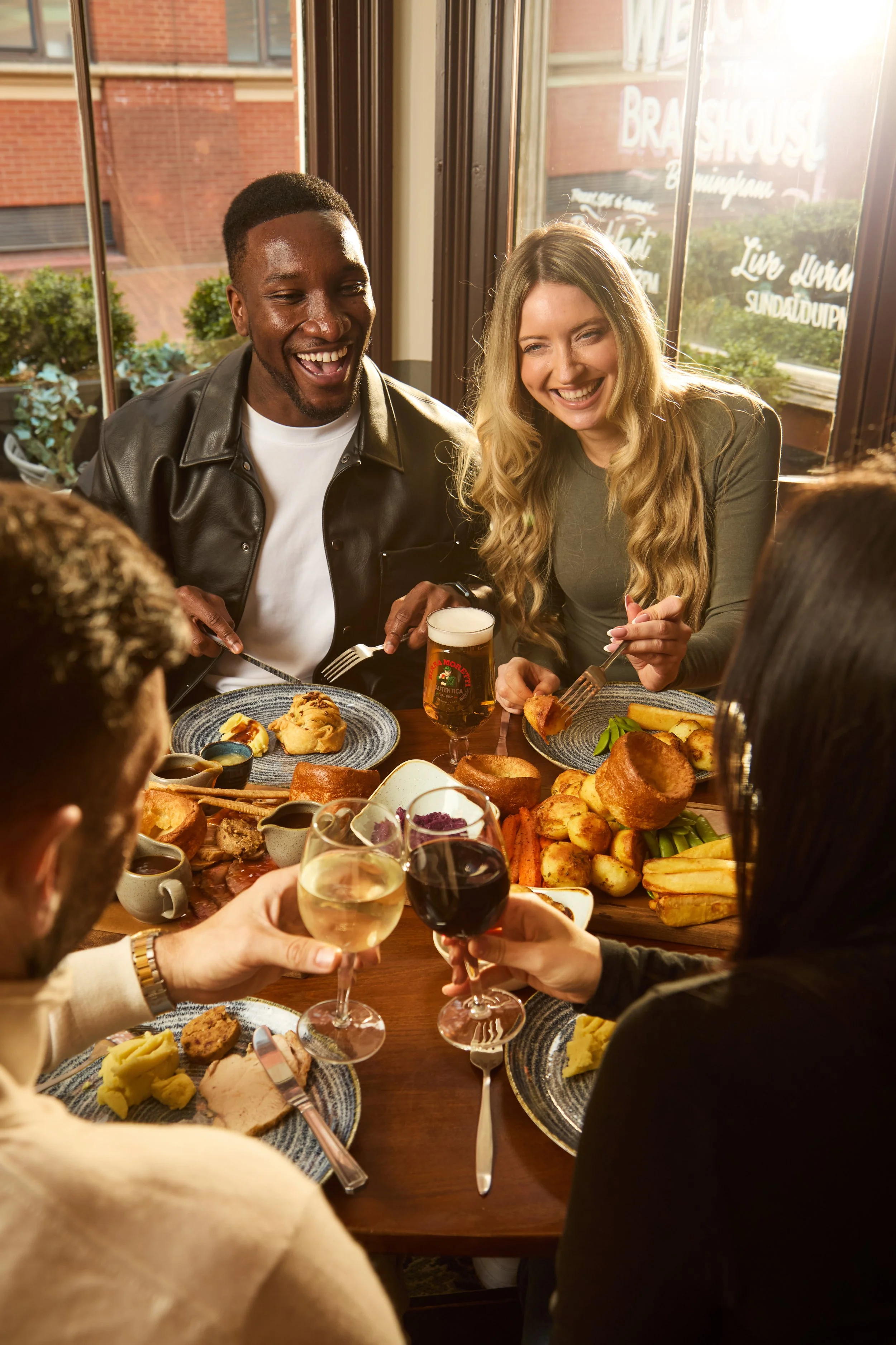 Group of people enjoying a meal at a restaurant with a large spread of food and drinks, smiling and toasting.