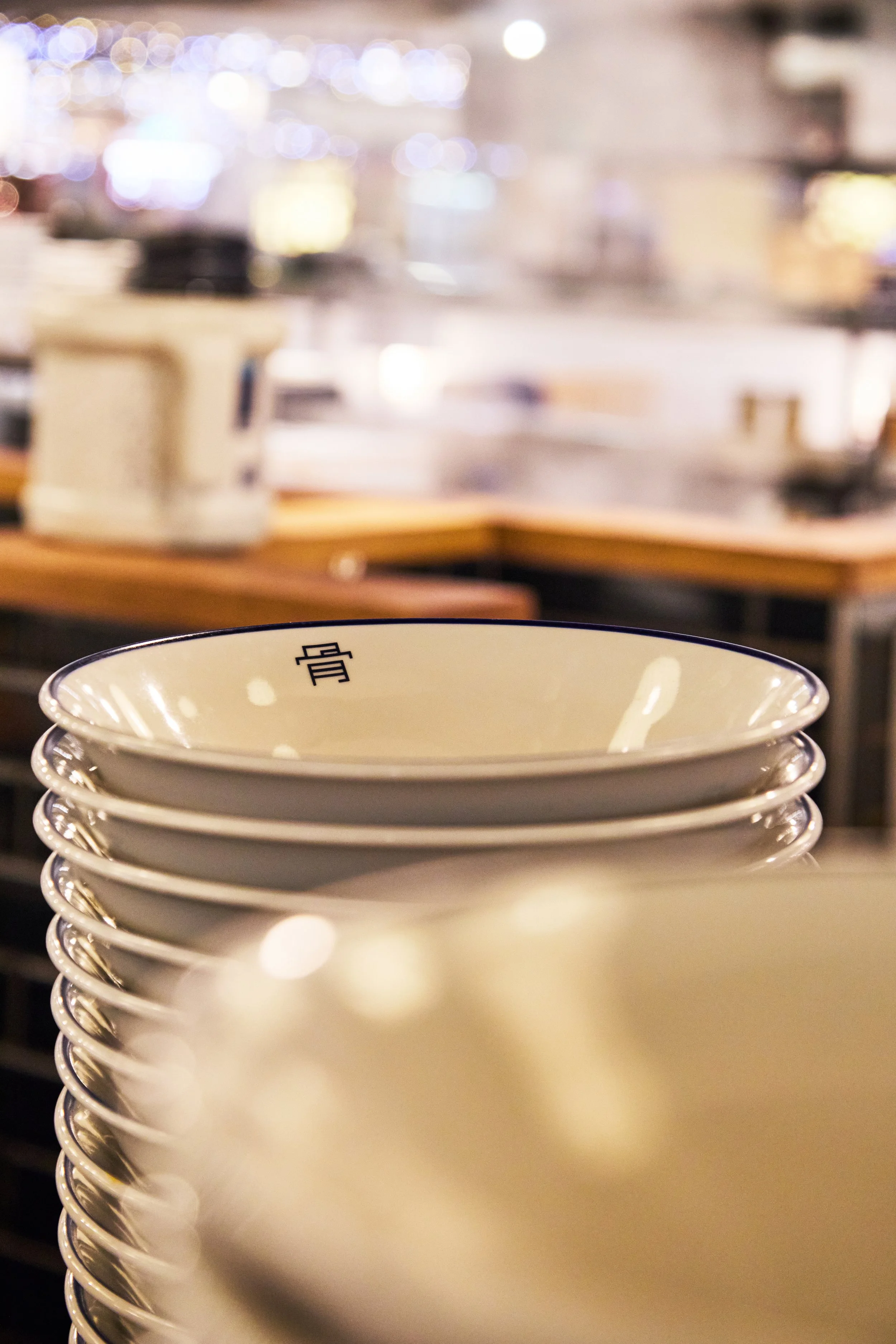 Stack of white ceramic bowls with black Chinese characters, in a restaurant setting.
