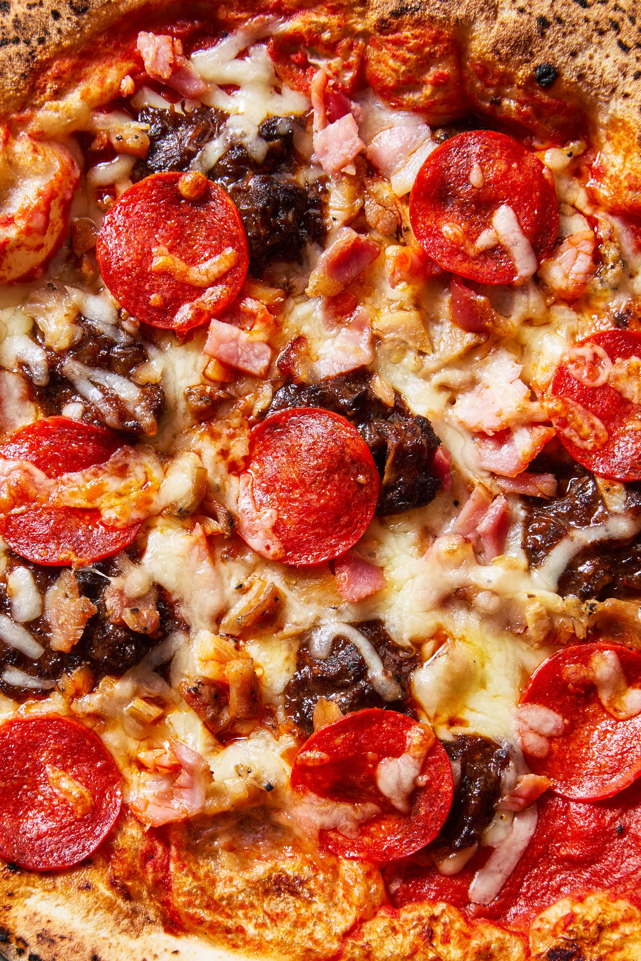 Close-up of a pizza with pepperoni, bacon, sausage, mushrooms, and melted cheese.