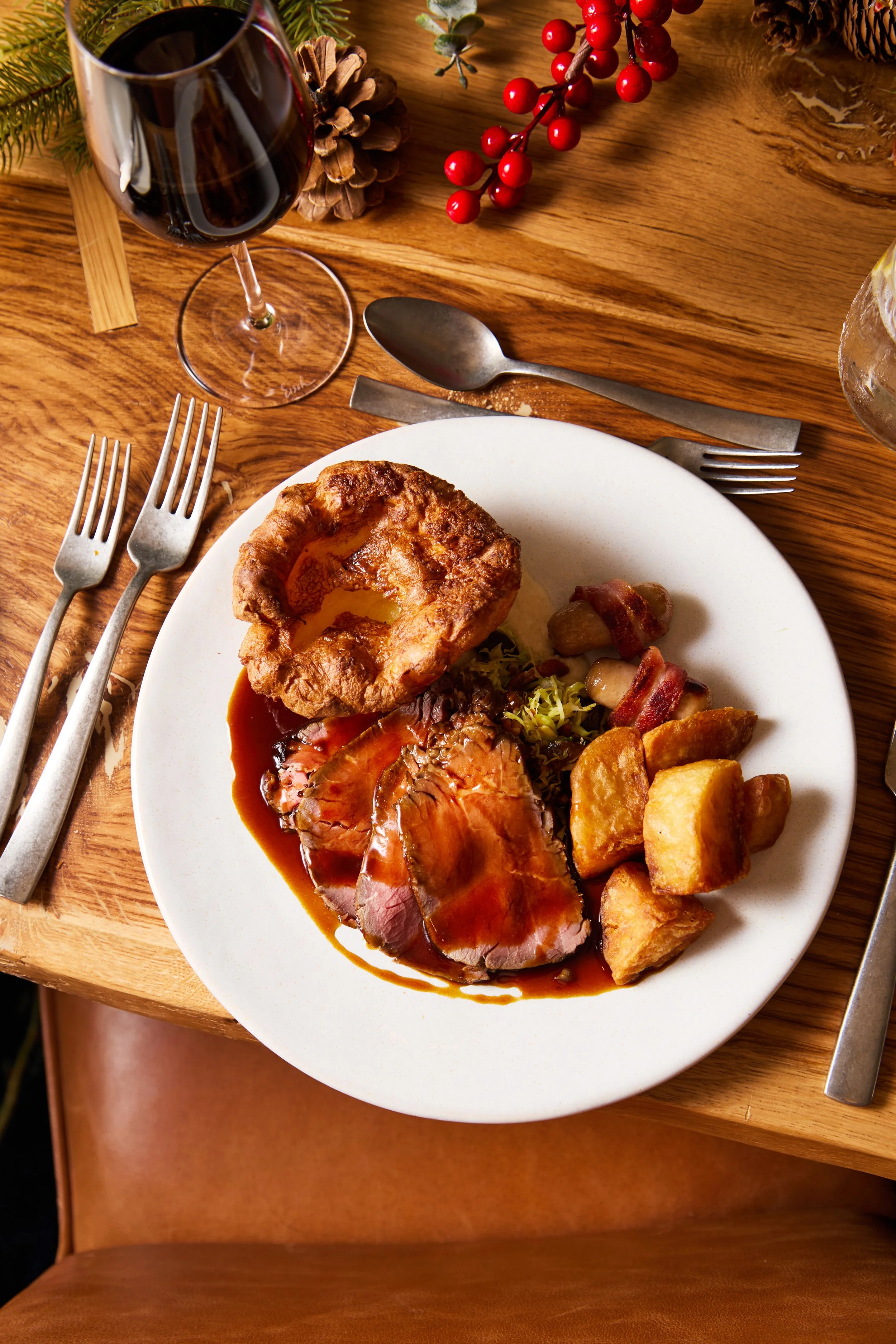 Plate of roasted turkey with gravy, stuffing, roasted potatoes, bacon-wrapped vegetables, and mashed potatoes, served with a glass of red wine at a holiday dinner setting.