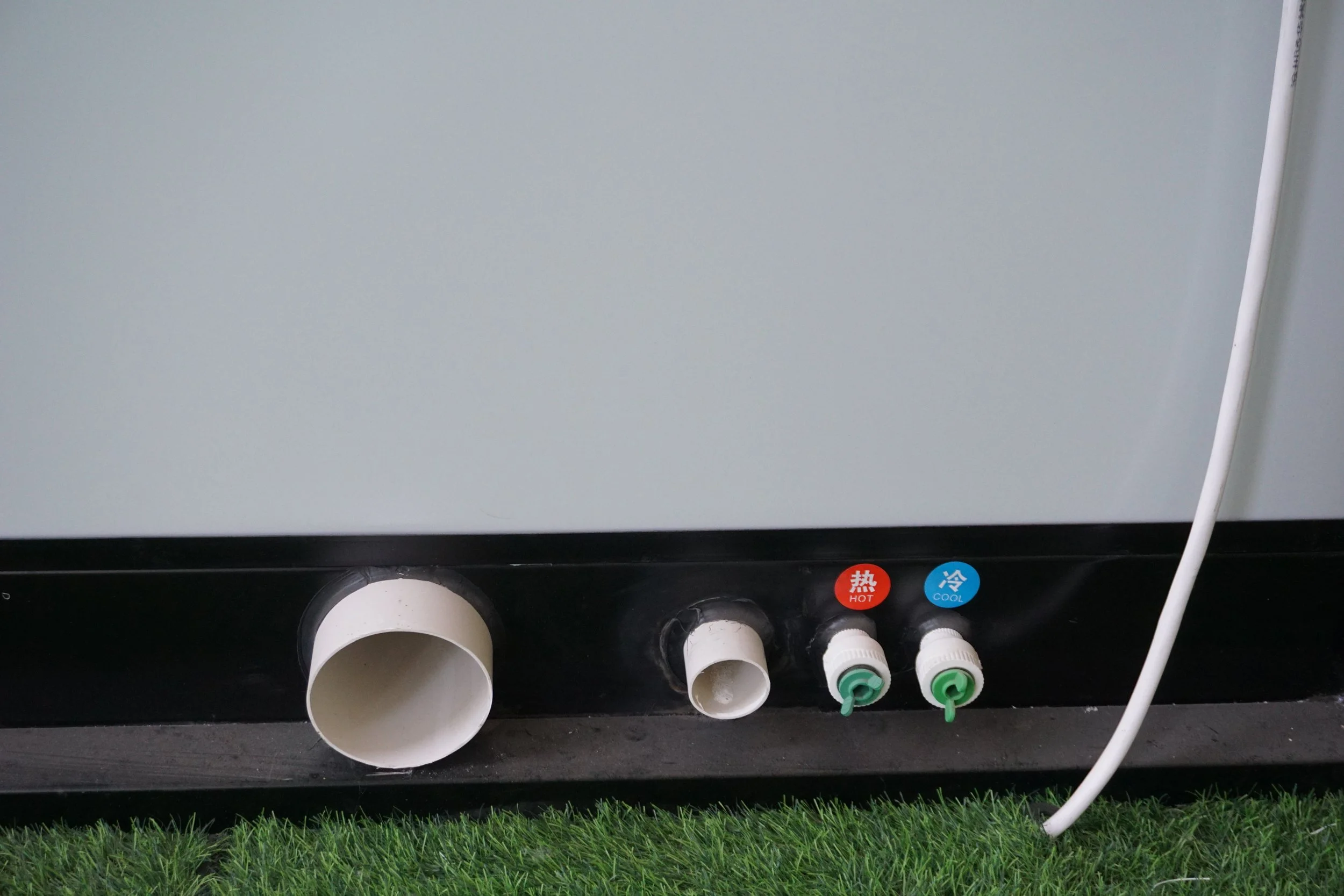 Close-up of the bottom part of a water dispenser or cooler with two white pipes, two labels indicating hot and cold water in Chinese, and a cable.