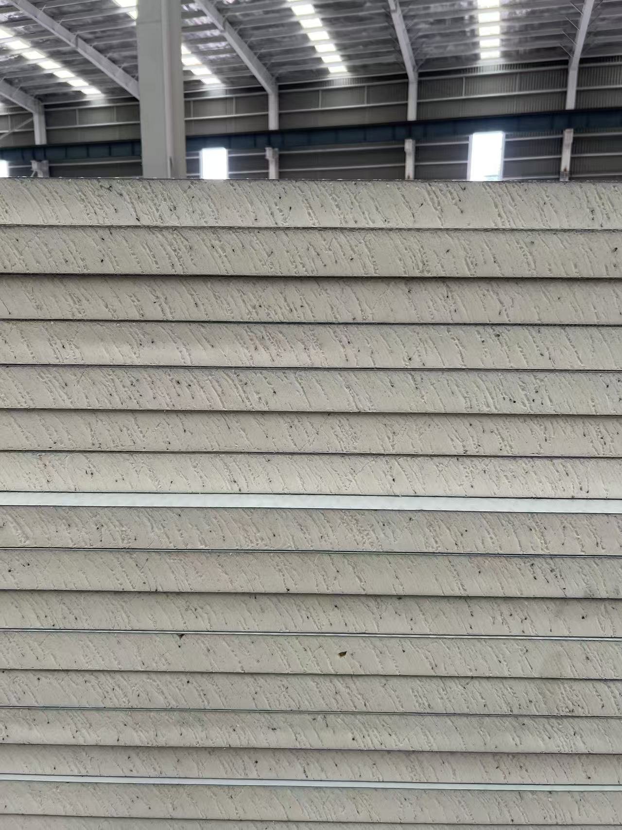 A large stack of striped, beige-colored panels inside an industrial warehouse.
