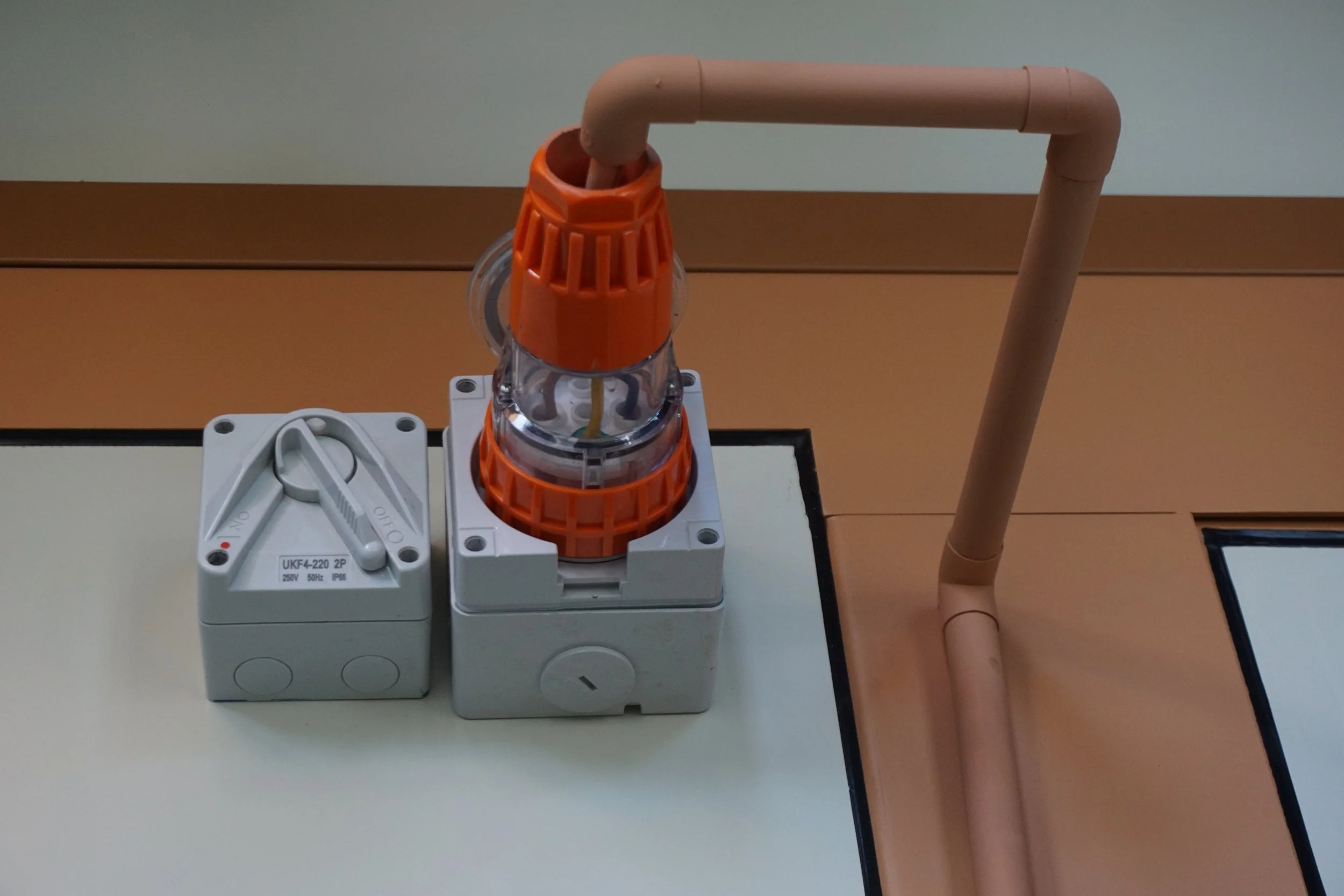 Electrical junction box with a switch and a safety isolator connected to a brown PVC pipe system.