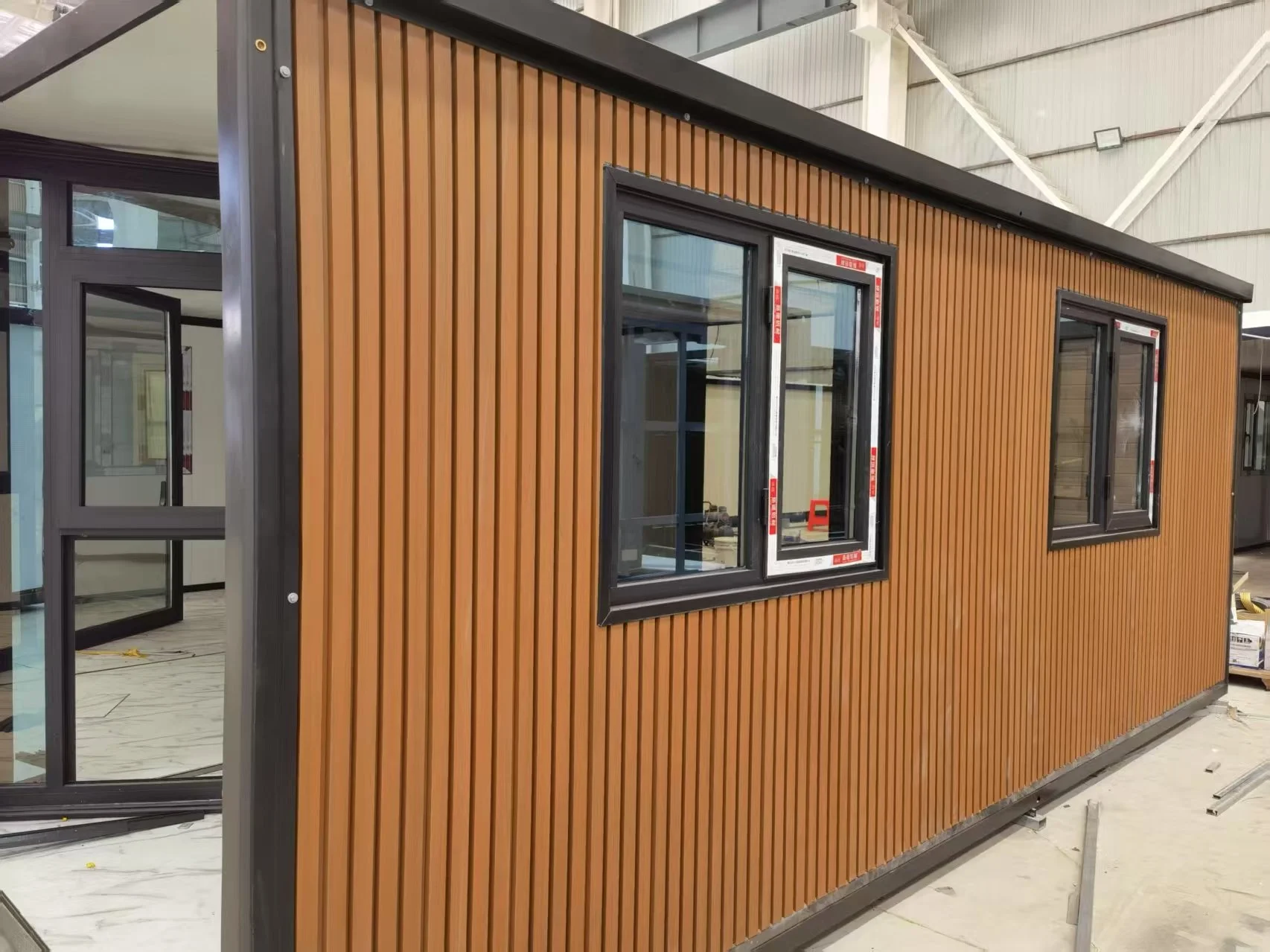 A wooden exterior building with black-framed windows inside a warehouse or construction site.