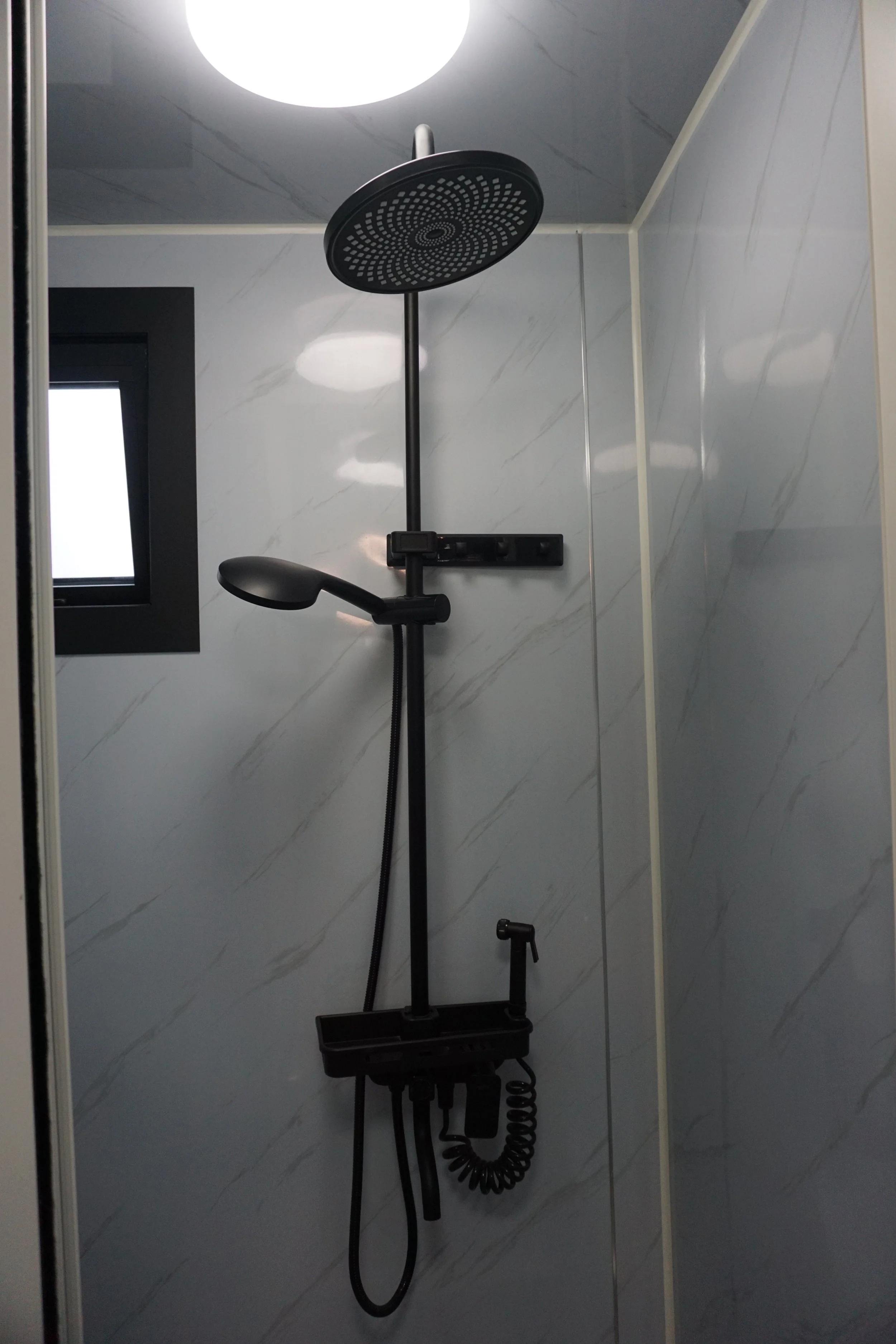 Shower area with a black rain shower head, hand shower, and a small window on a tiled wall.