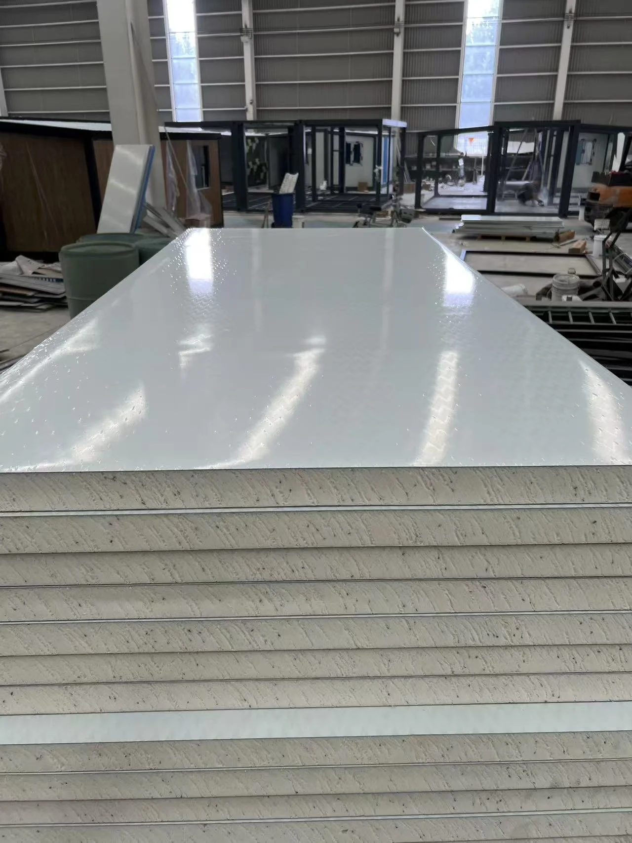 Stacks of white and beige materials, possibly foam or insulation panels, in an industrial warehouse setting with large windows and metal walls.
