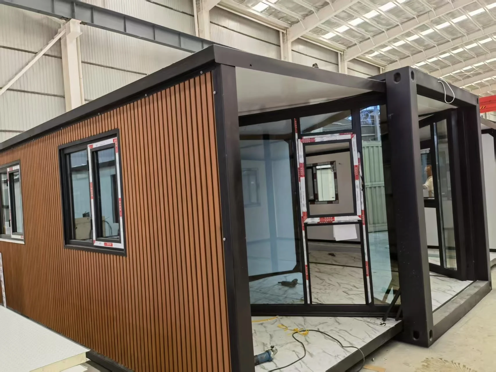 Interior of a modern tiny house or portable building under construction, with large windows and a wooden exterior wall paneling.