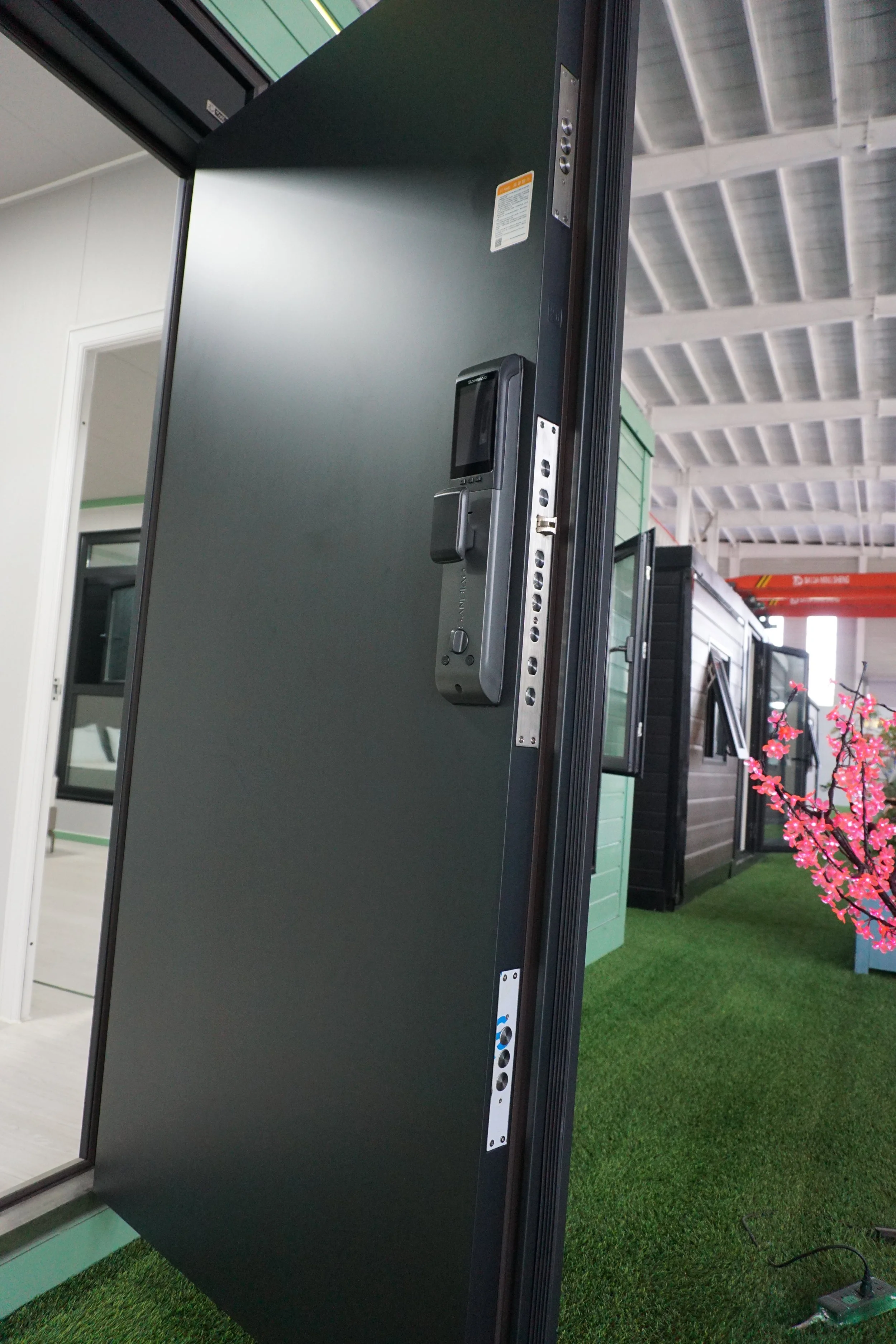 A large, black digital billboard with a digital camera mounted on it, standing indoors on artificial green grass.