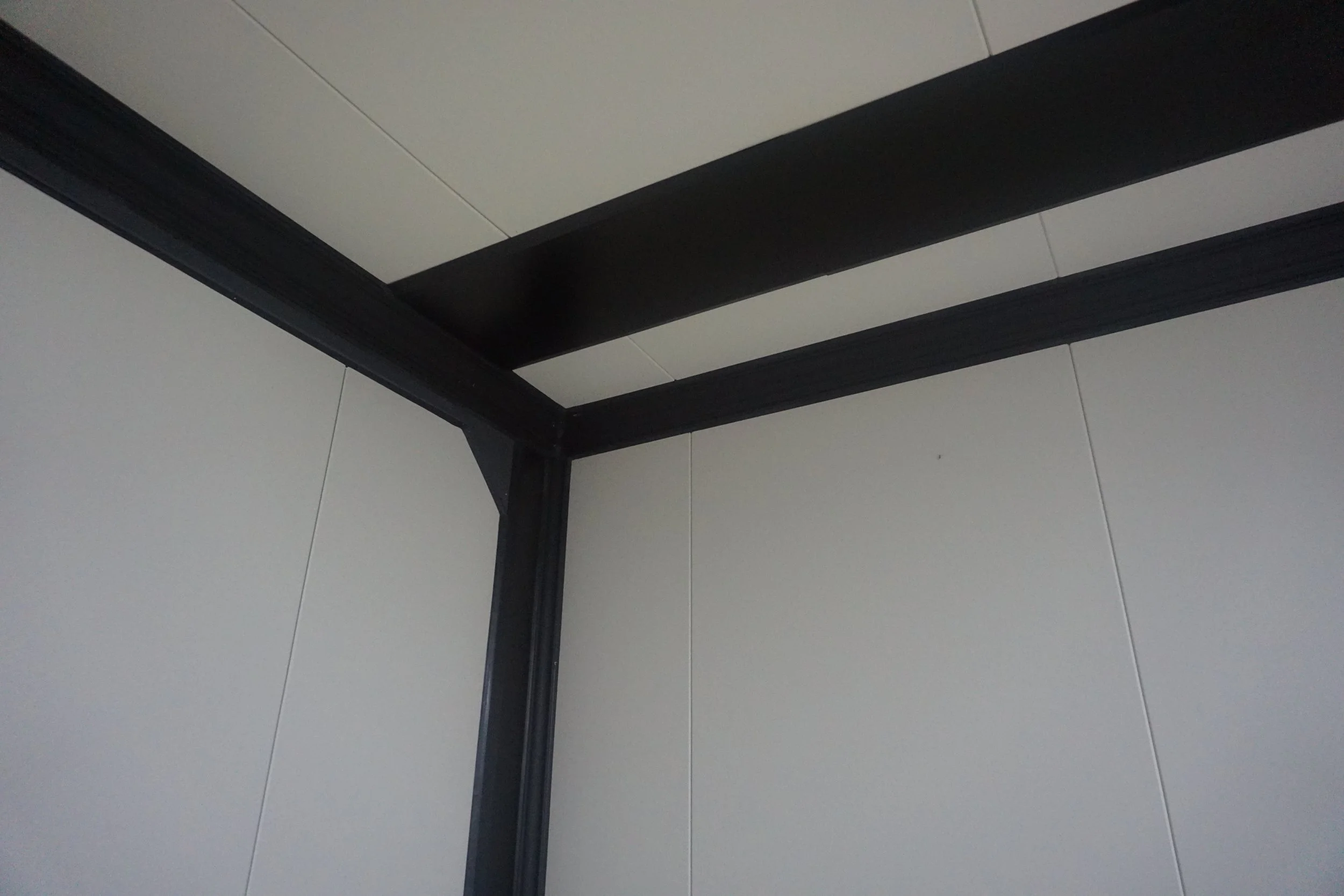 Corner of a room showing a black metal frame structure and white wall panels.