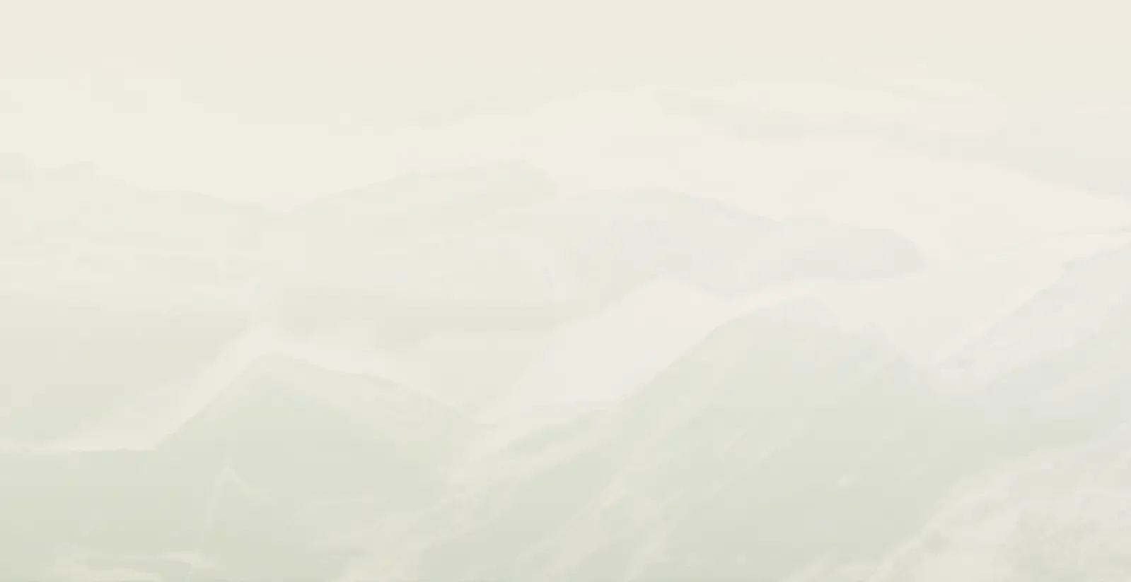 Soft, foggy mountain landscape with layered ridges fading into distance under a pale, overcast sky.
