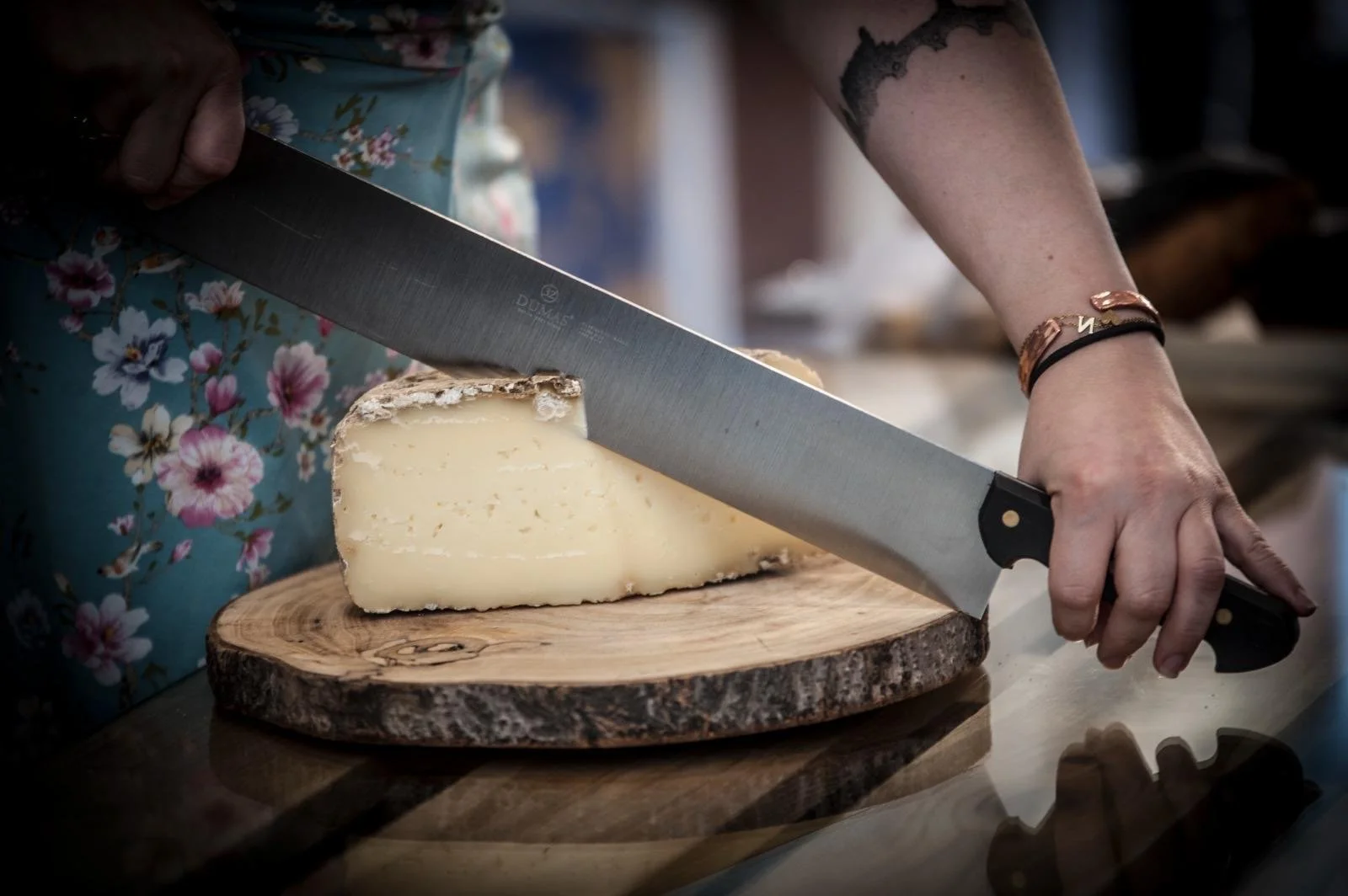 Une personne coupe du fromage à pâte dure sur une planche en bois avec un grand couteau.