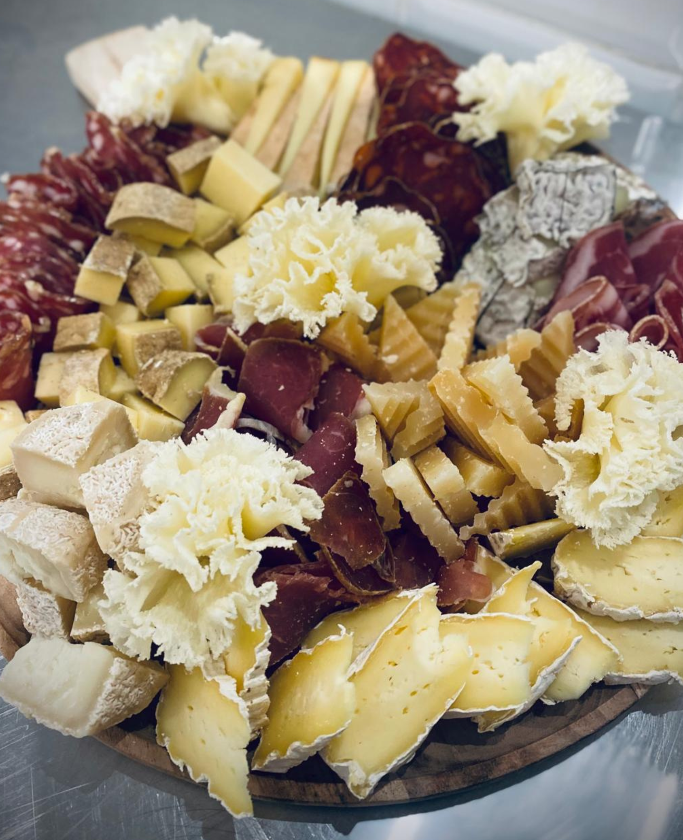 Plate de fromages variés, avec différentes textures et couleurs, garnie de charcuterie et de légumes.