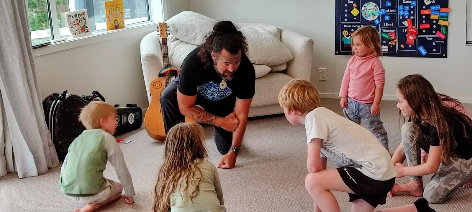 Matiu teaching haka to Earth School children at one of our indoor facilities. There is a window with books on the window sill. A colorful educational poster is on the wall.
