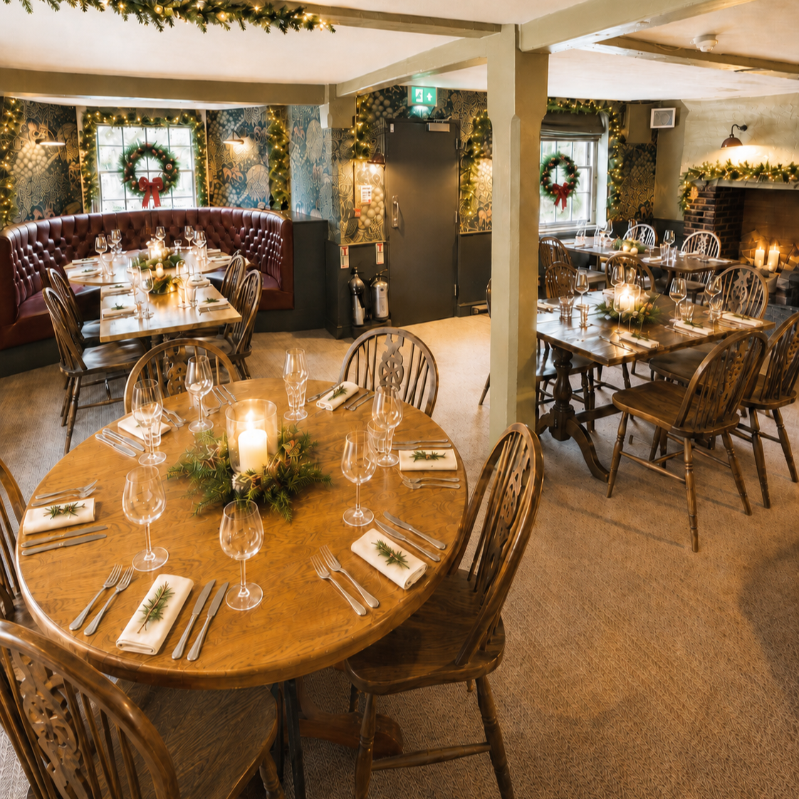 A cozy, festively decorated restaurant with wooden tables and chairs, Christmas wreaths, fairy lights, a fireplace with candles, and a large round table with a candle centerpiece, prepared for holiday dining.