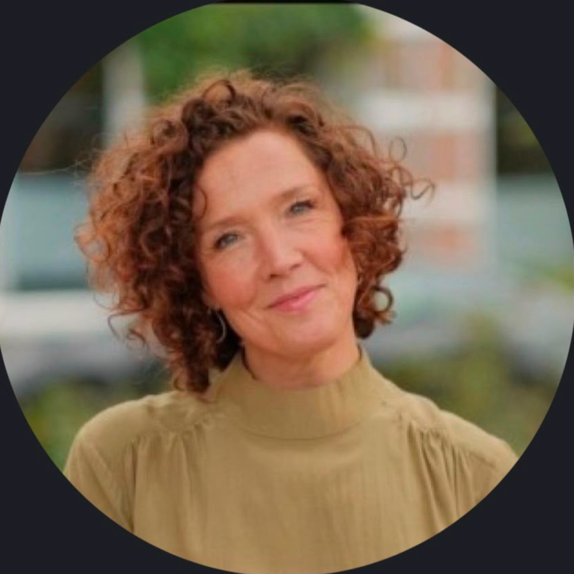 Een vrouw met gekrulde, bruinrode haar die glimlacht, buiten met een groene achtergrond.