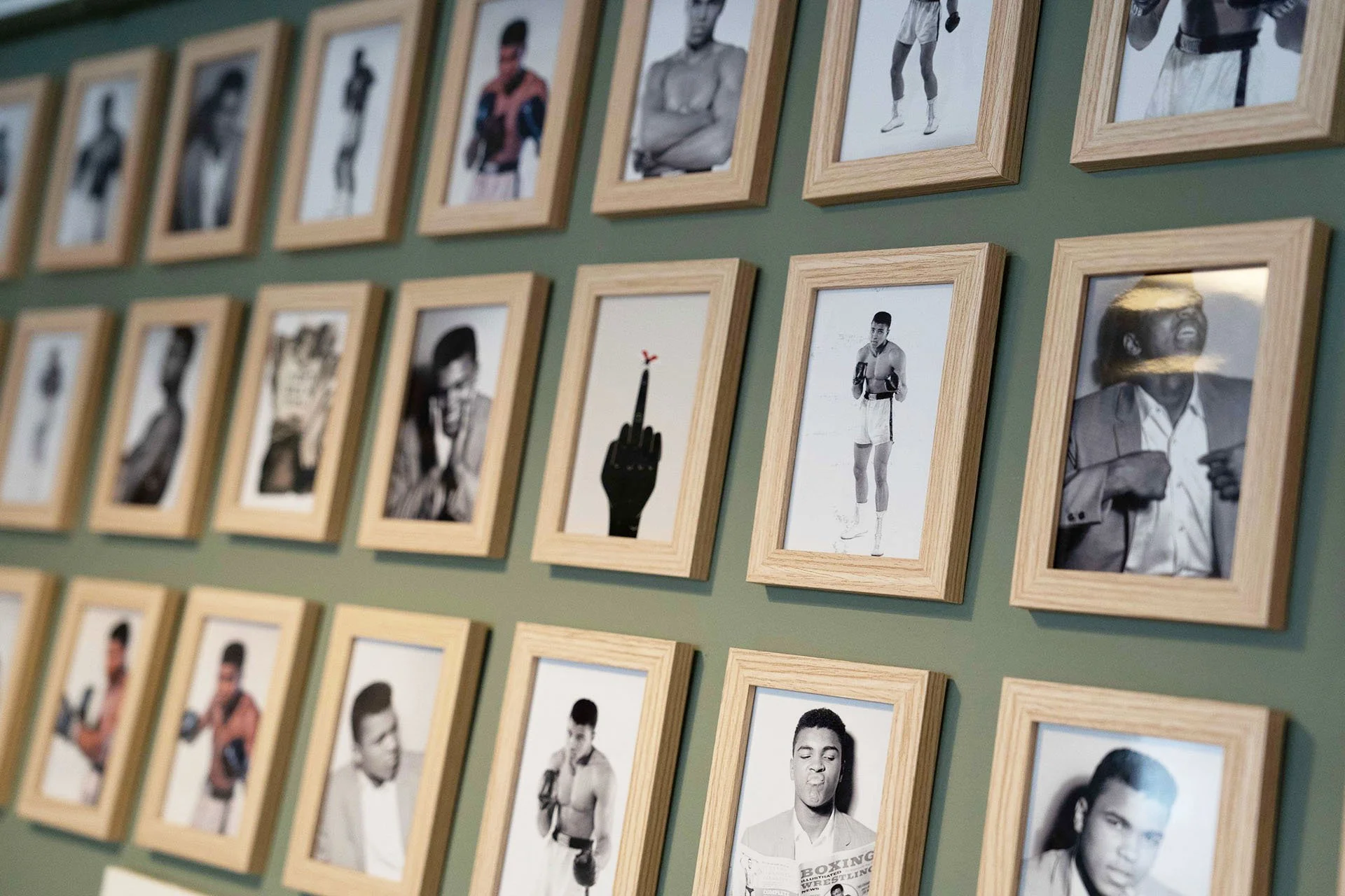 Wall display of framed black-and-white photographs of boxers, with one artistic photo of a hand with a bird on its middle finger.