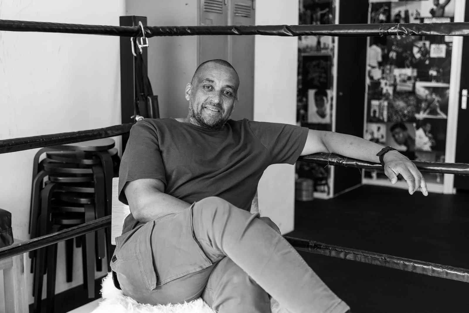 Man zittend in een sportschool naast een bokszak, zwart-wijn foto, glimlachend.