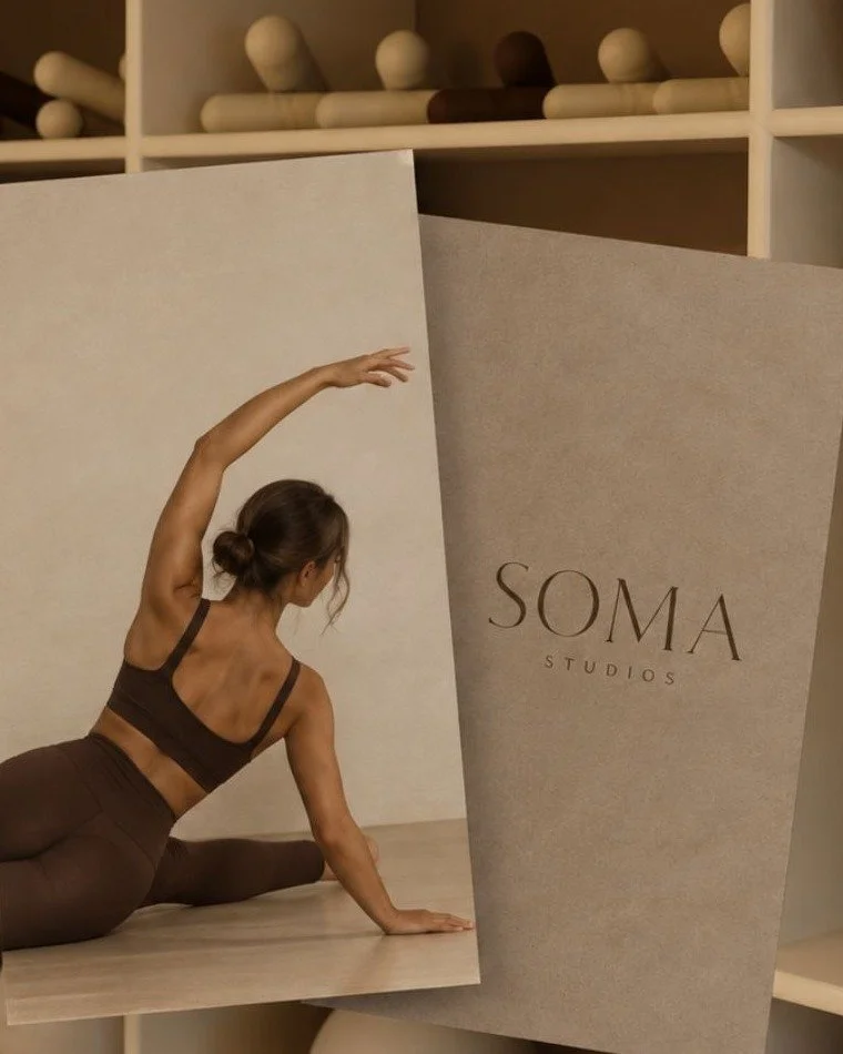 Woman stretching in a side bend beside a Soma Studios card on the studio shelves