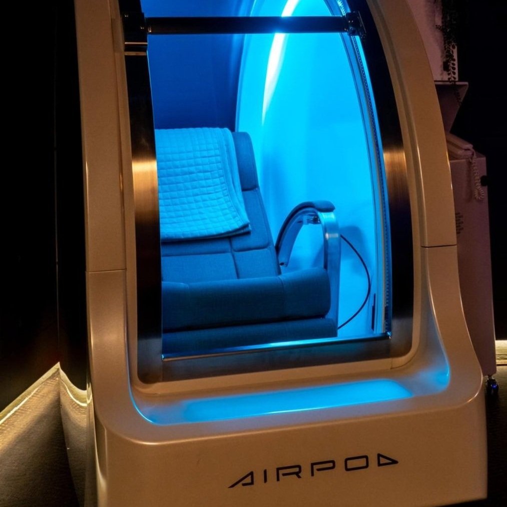 A white and gold futuristic-looking capsule or pod with the word 'AIRPOD' written on it, situated on a wooden surface with warm lighting.
