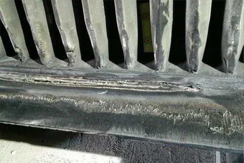 Close-up of a dirty, worn car radiator grille with a damaged lower trim piece.
