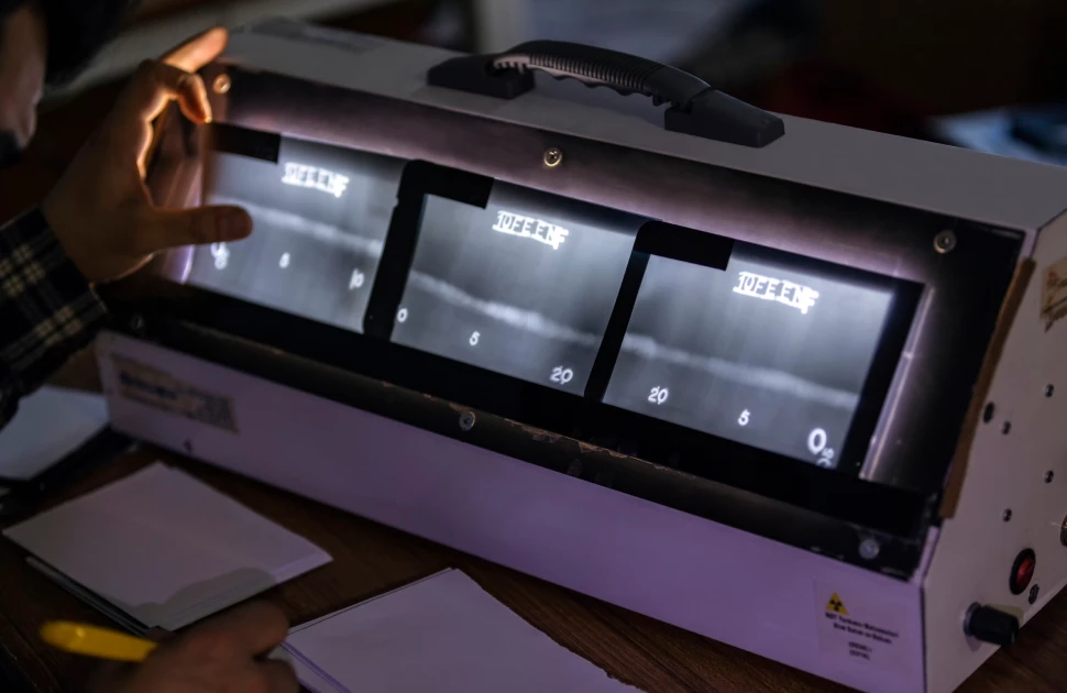 A person operating a Geiger counter device with a black display showing radiation levels in a dark room.