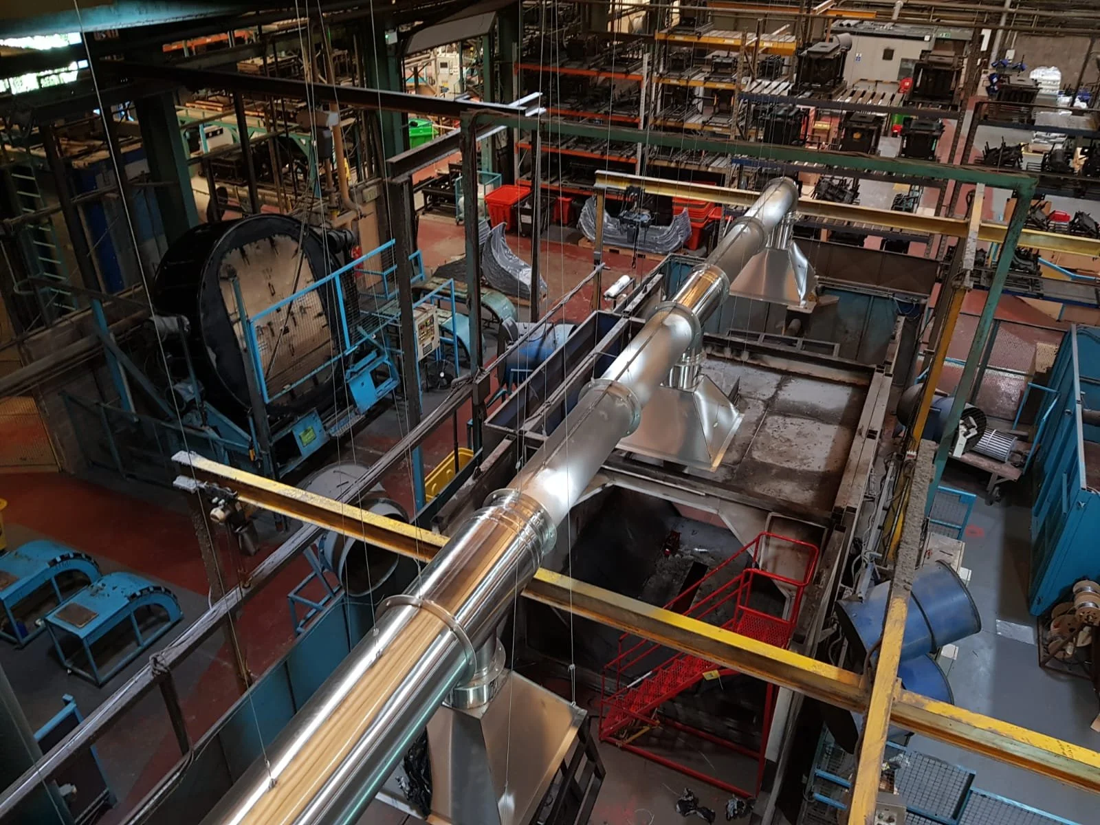An industrial factory interior with metal piping, machinery, and equipment, viewed from above.