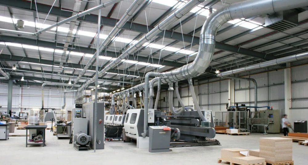 Inside a manufacturing factory with large industrial machines and ventilation ducts.