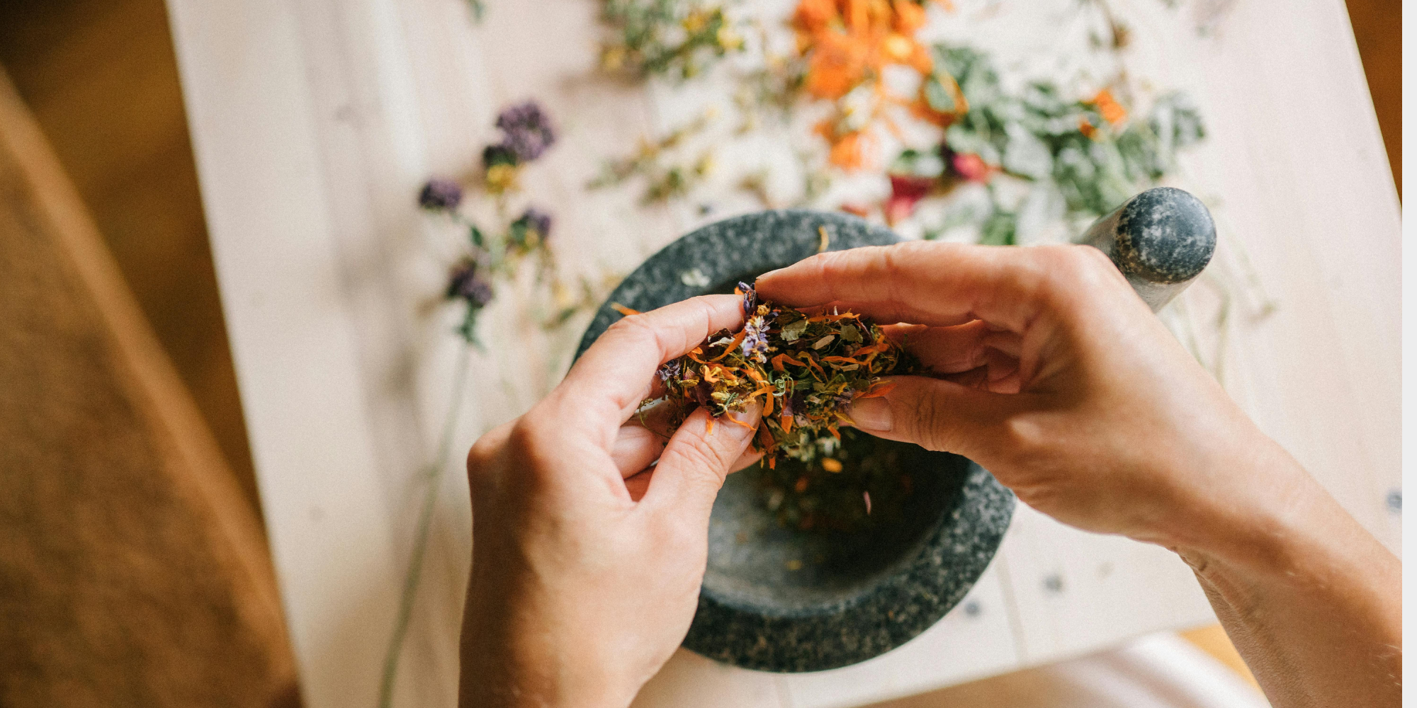 Close up of a pair of hands rubbing together floral, herbal remedies into the granite mixing bowl.