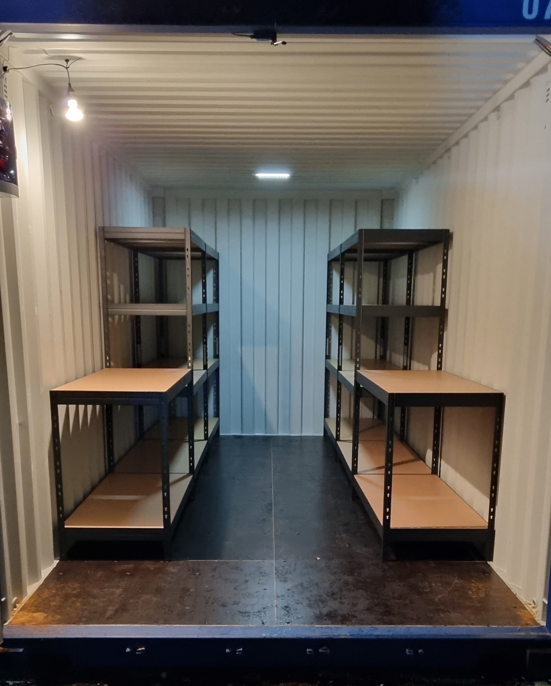 Empty storage unit with metal shelving on both sides and ceiling lights.