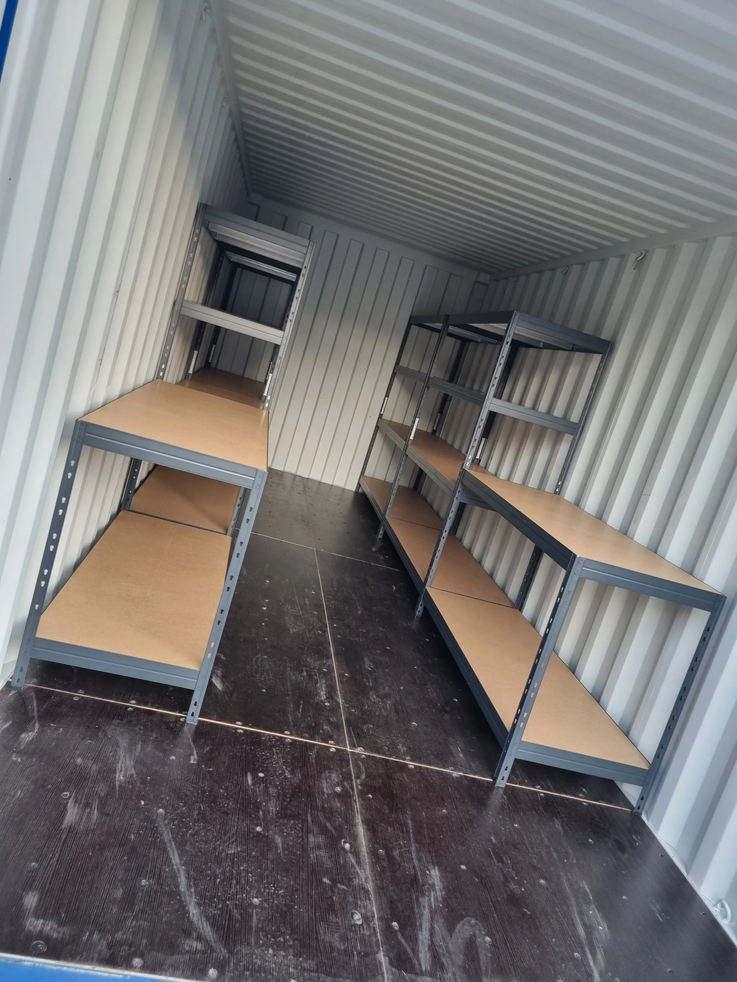 Empty storage unit with metal shelving and wooden shelves inside.