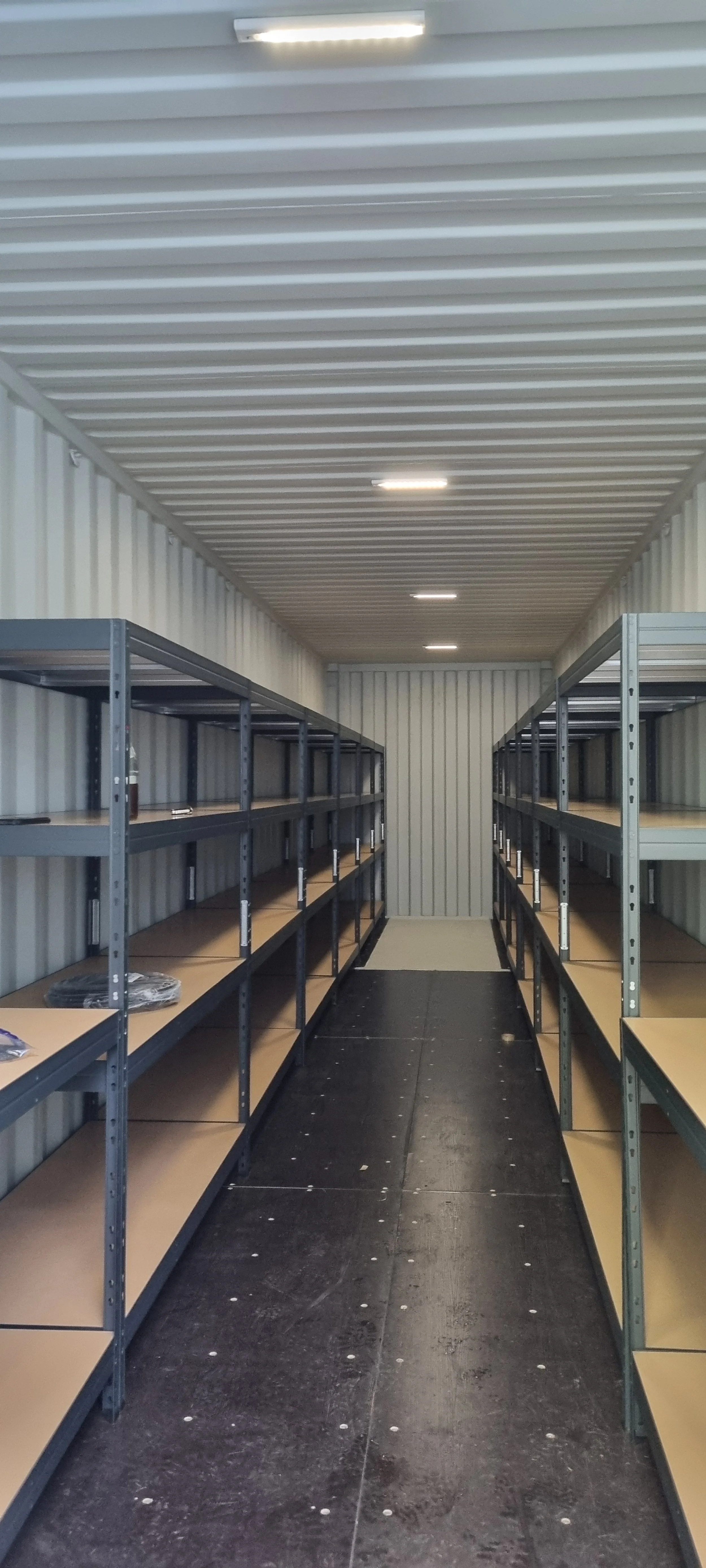 Empty storage unit with metal and wooden shelves on both sides and a black floor.