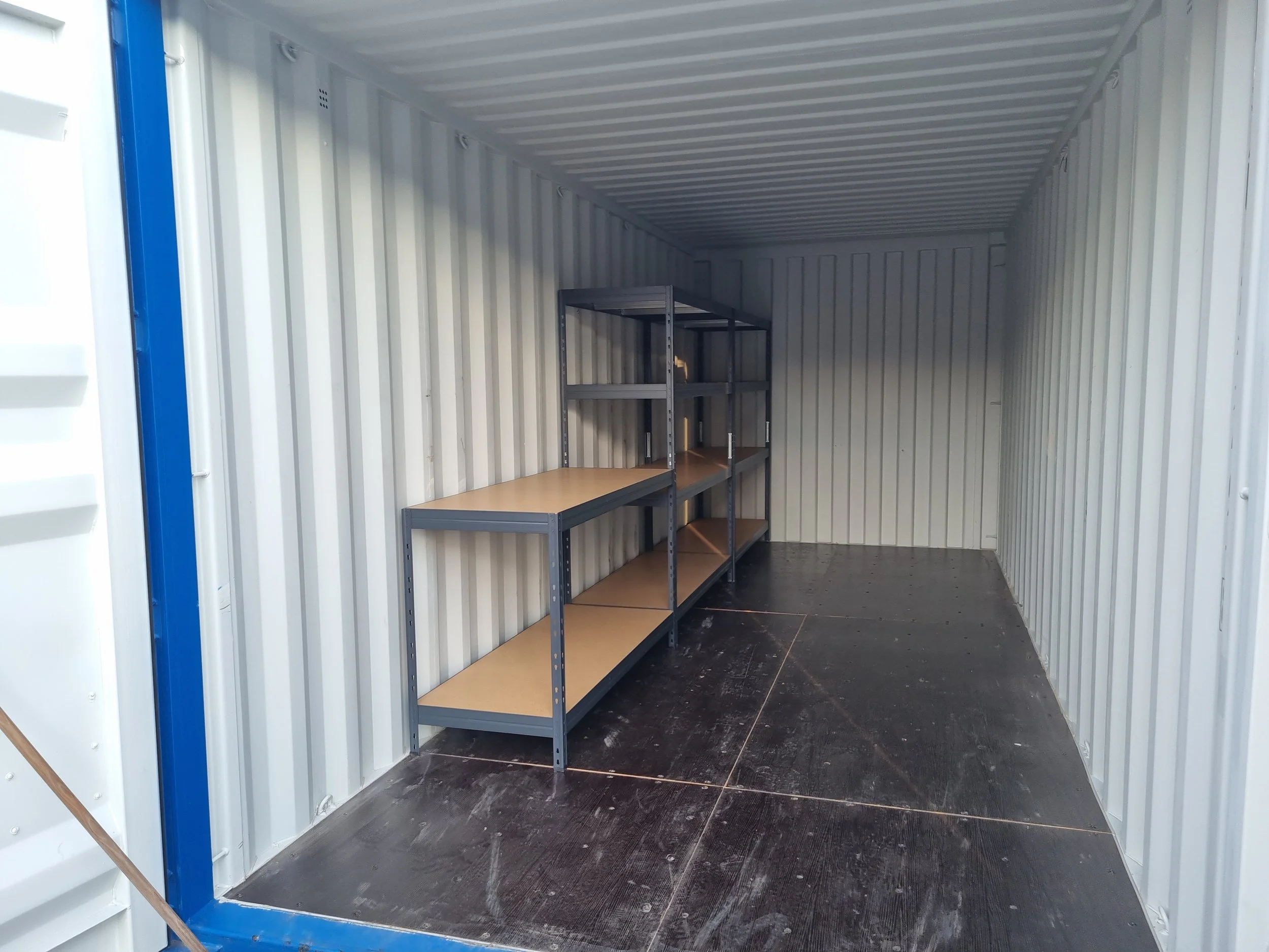 Empty storage container with metal shelving unit along the left wall, interior with metal walls, flooring, and ceiling.