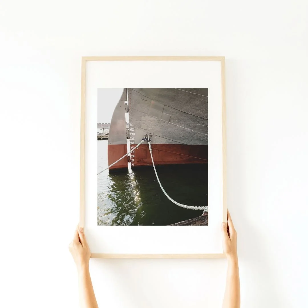 Photo of a large ship docked at a port, with a person holding a framed photo of the ship in front of it.