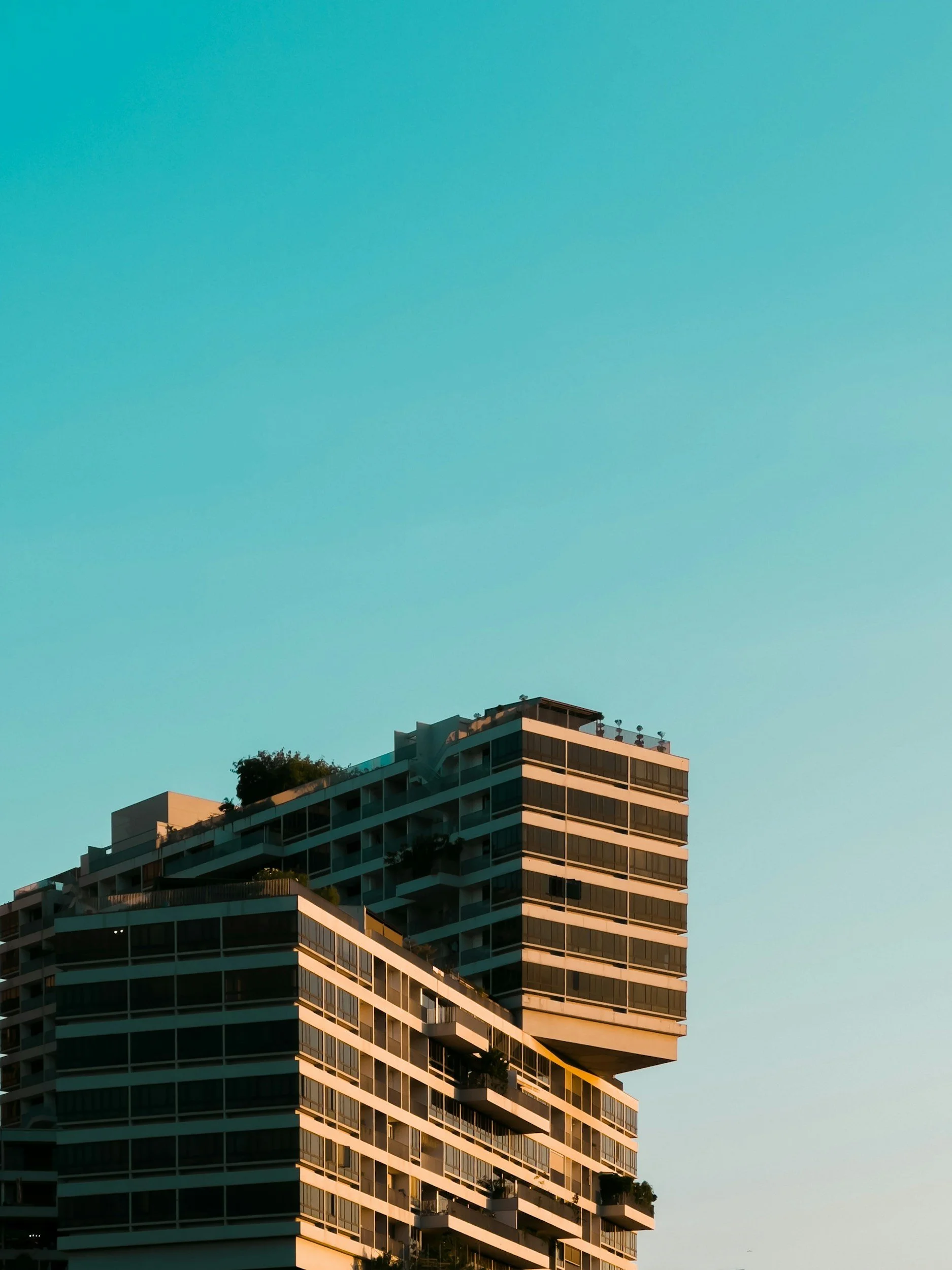 Modern multi-story apartment building Interlace with balconies and rooftop greenery against a clear blue sky
