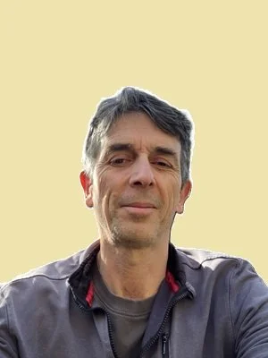 A man with gray hair wearing a dark jacket against a light yellow background.
