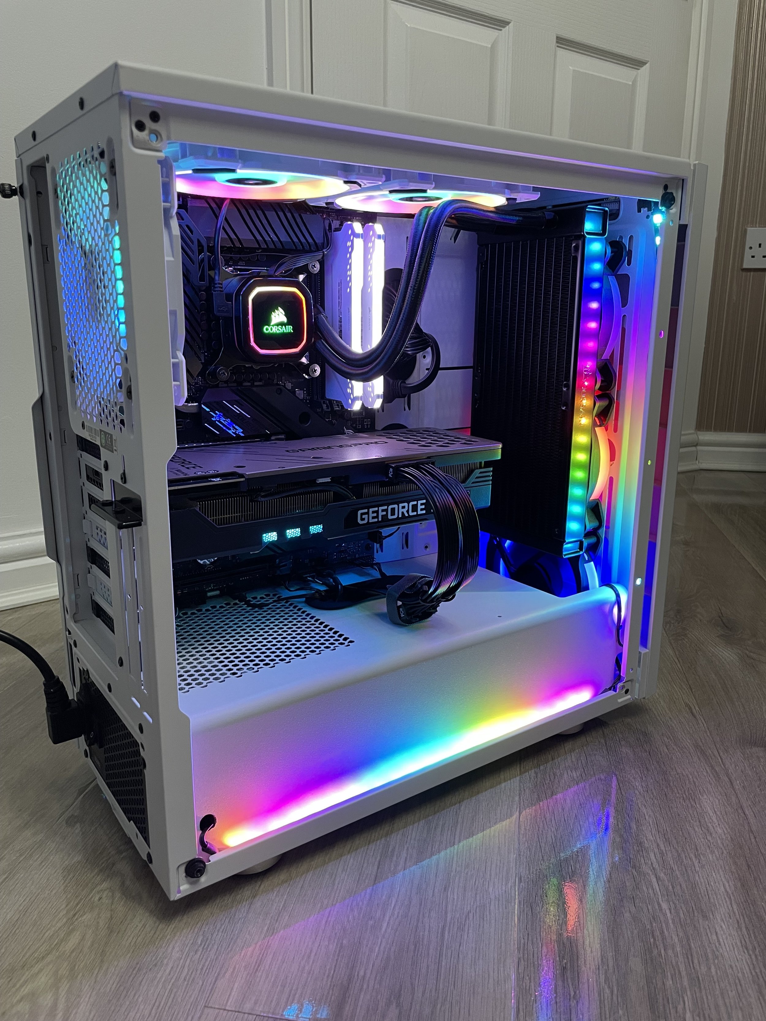 A custom-built gaming computer with a white case, RGB lighting, water cooling system, GeForce graphics card, and illuminated cooling fans.