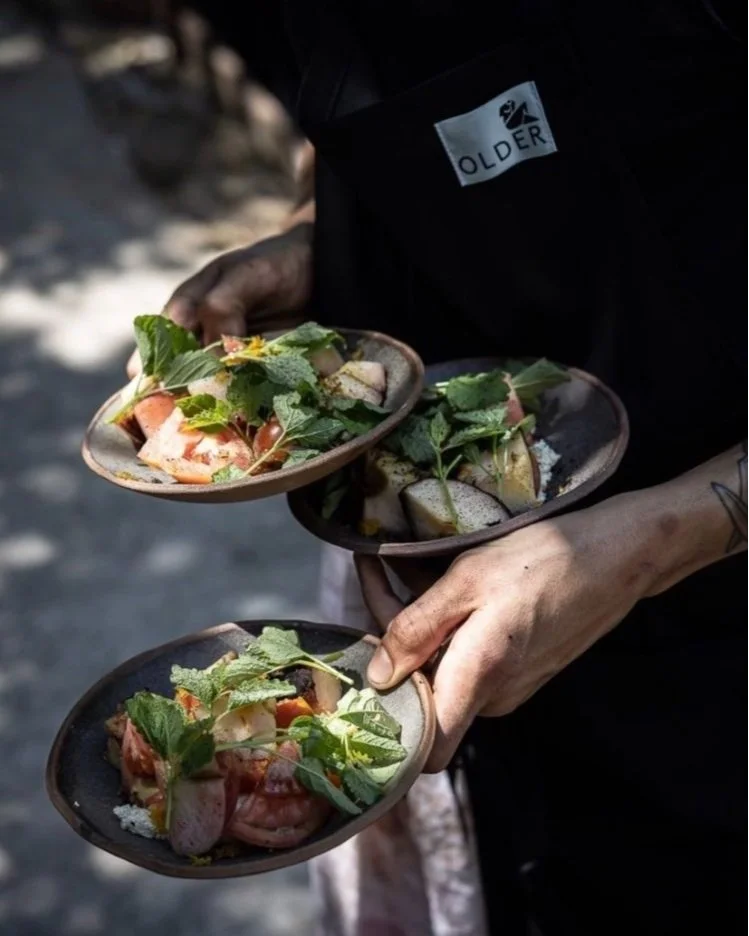 Une personne tient trois assiettes avec des plats composés de légumes, de fruits et de feuilles de menthe.