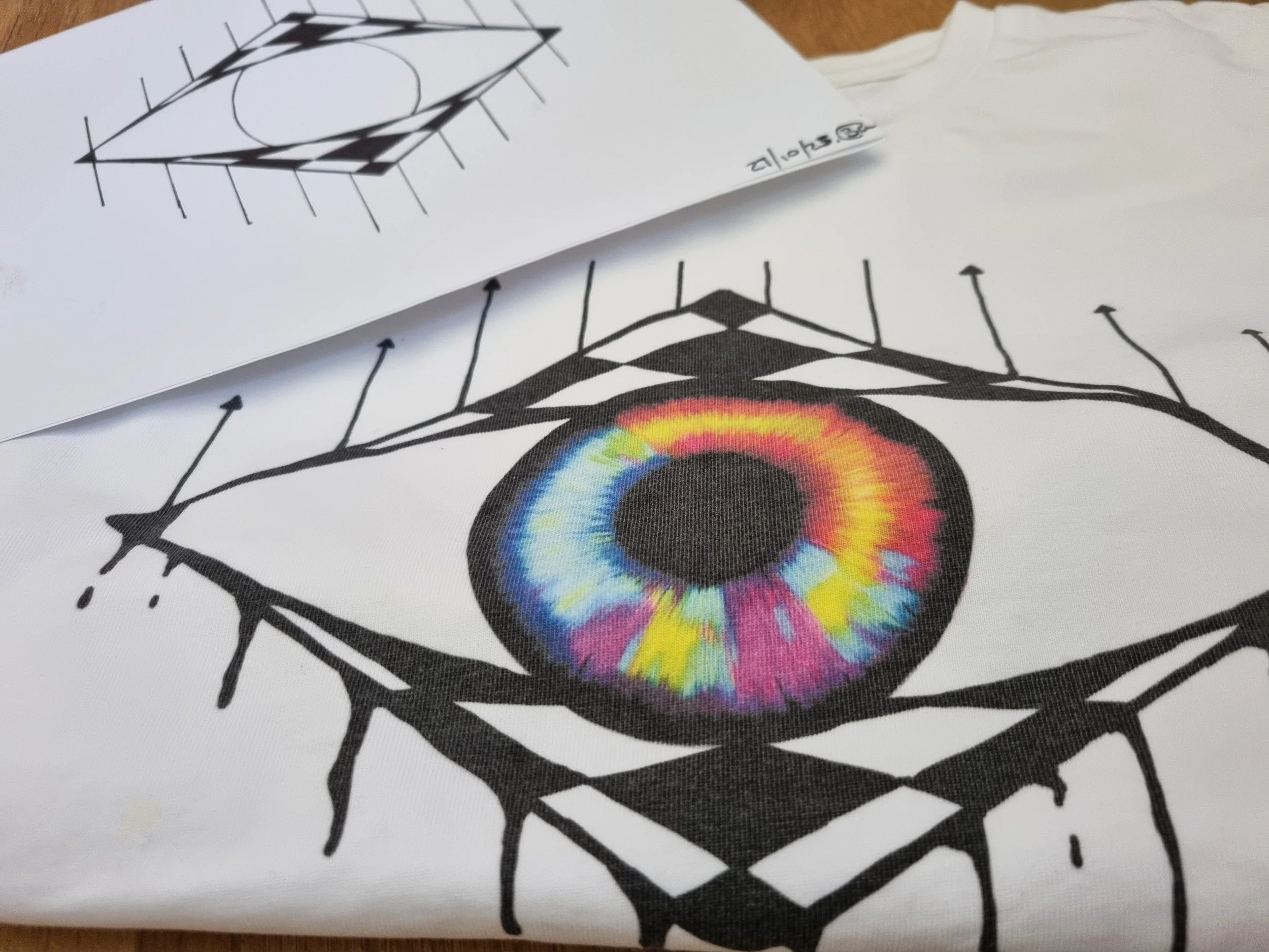 Original Mongrel Logic eye drawing beside the finished multicoloured eye print on an organic cotton T-shirt